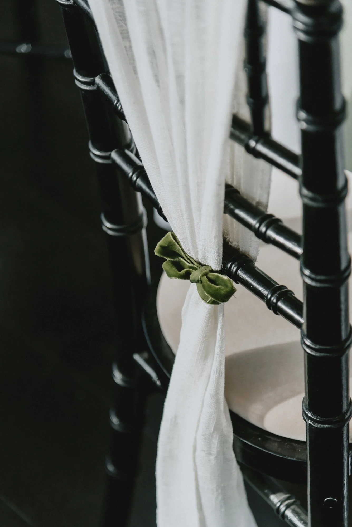 Close-up of a white curtain tied back with a green fabric bow, seen through the black wooden spindles of a chair.