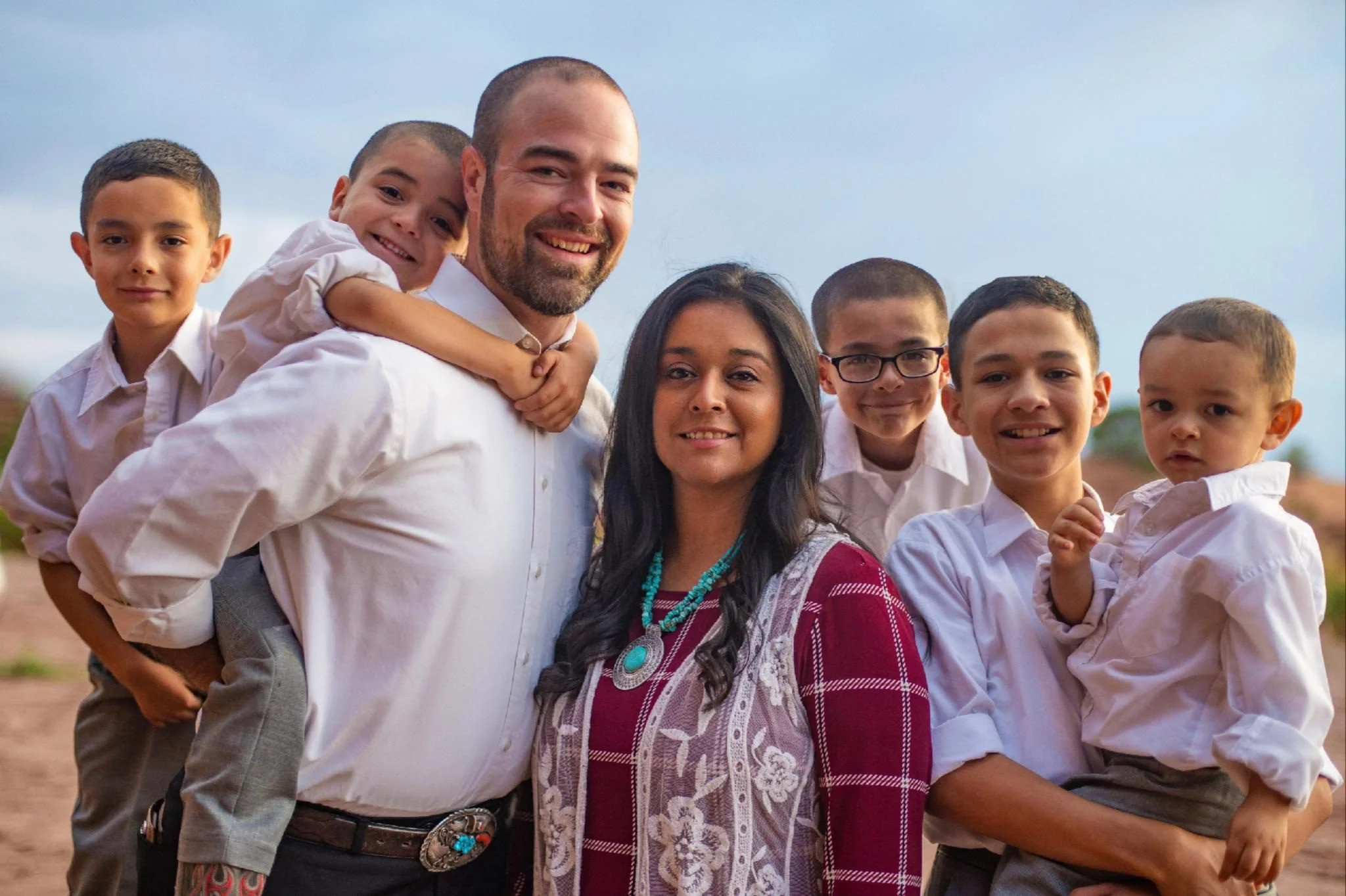 A family of seven, including two adults and five children, standing outdoors during daytime with a cloudy sky in the background.
