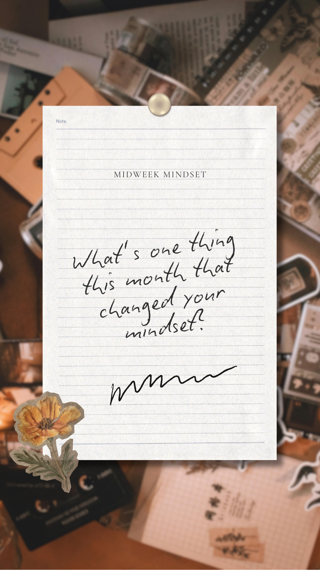 A notepad with the title 'Midweek Mindset' and a written message asking about how someone's mindset has changed this month, decorated with a flower sticker, on a background of various papers, tickets, and stationery items.