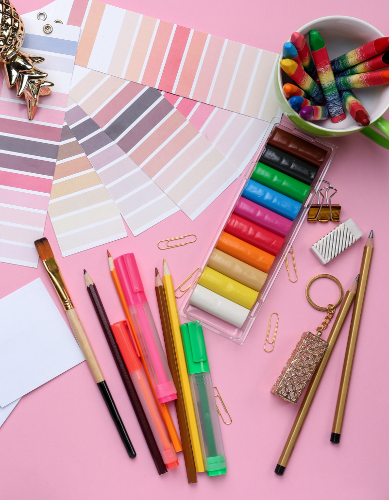 Creative art supplies including markers, pencils, paintbrushes, and color swatches arranged on a pink background.