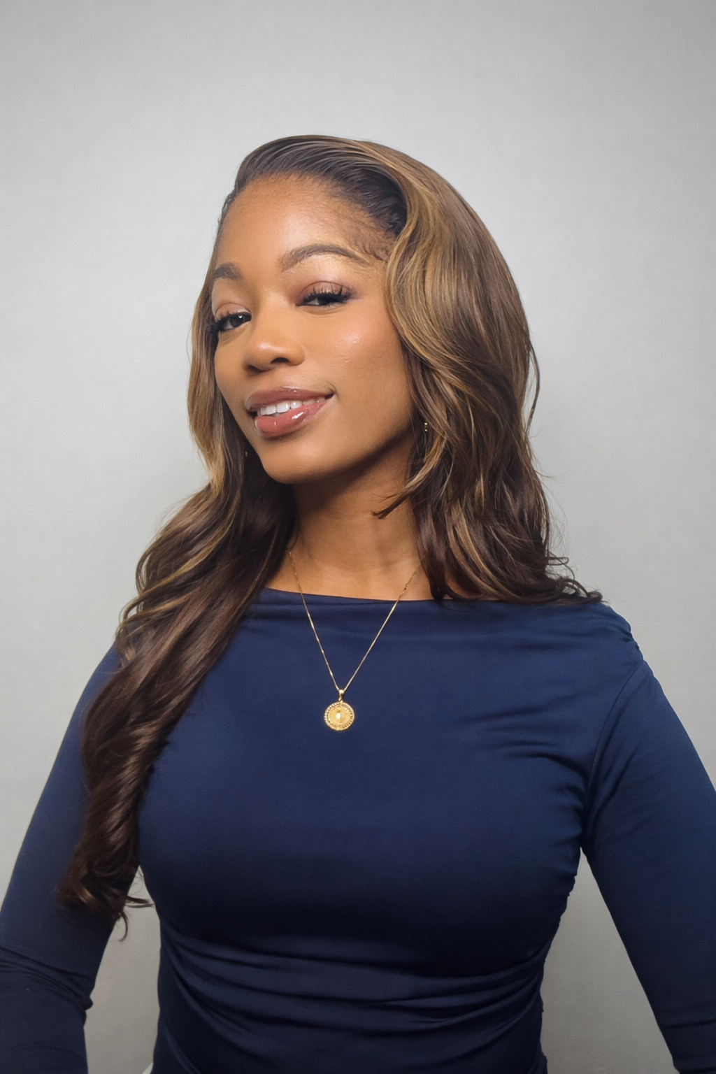 Professional headshot of a woman with long wavy hair wearing a blue top and gold necklace against a neutral background.