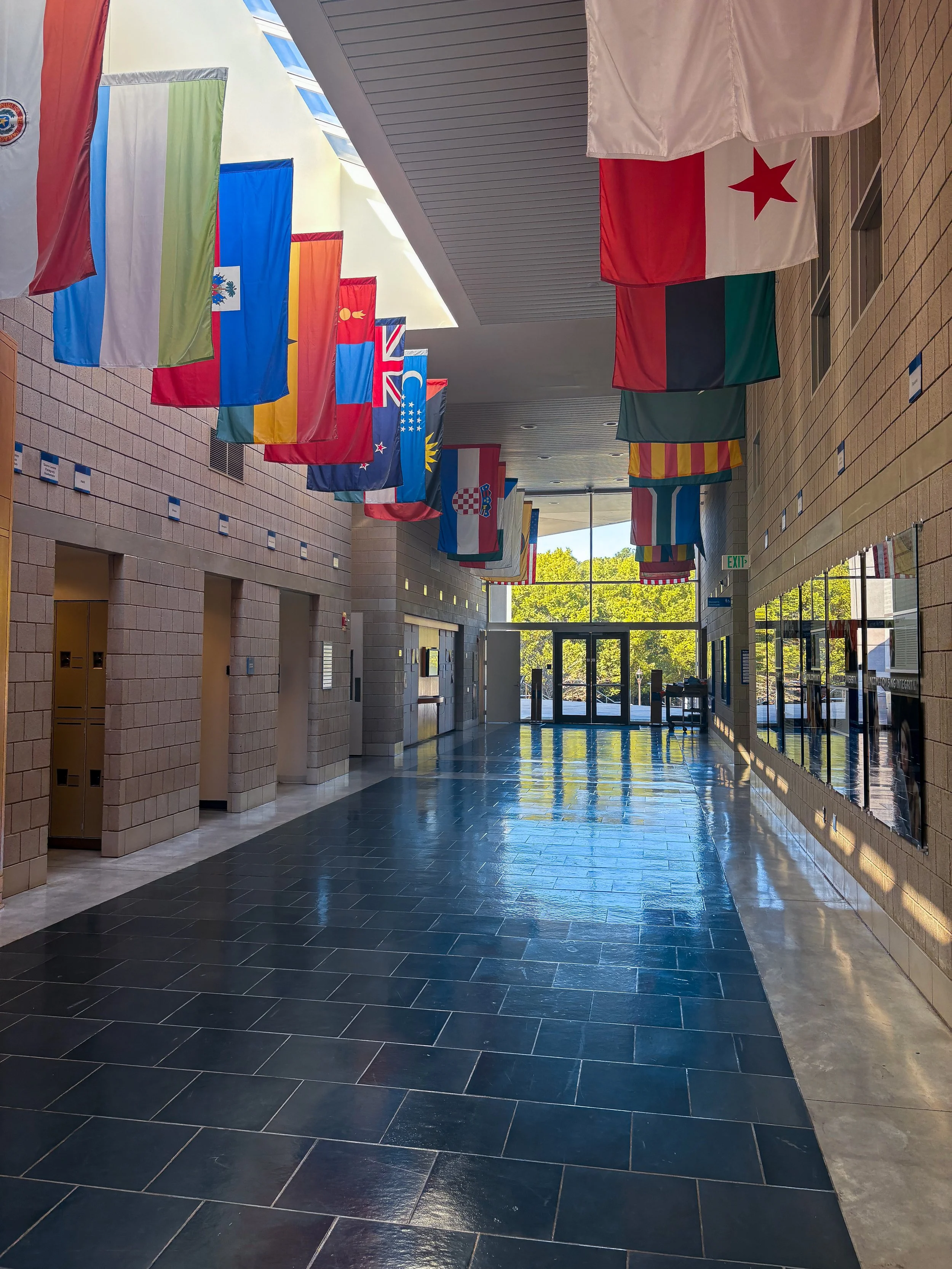 Indoor hallway with international flags hanging from the ceiling and natural sunlight reflecting through large windows.