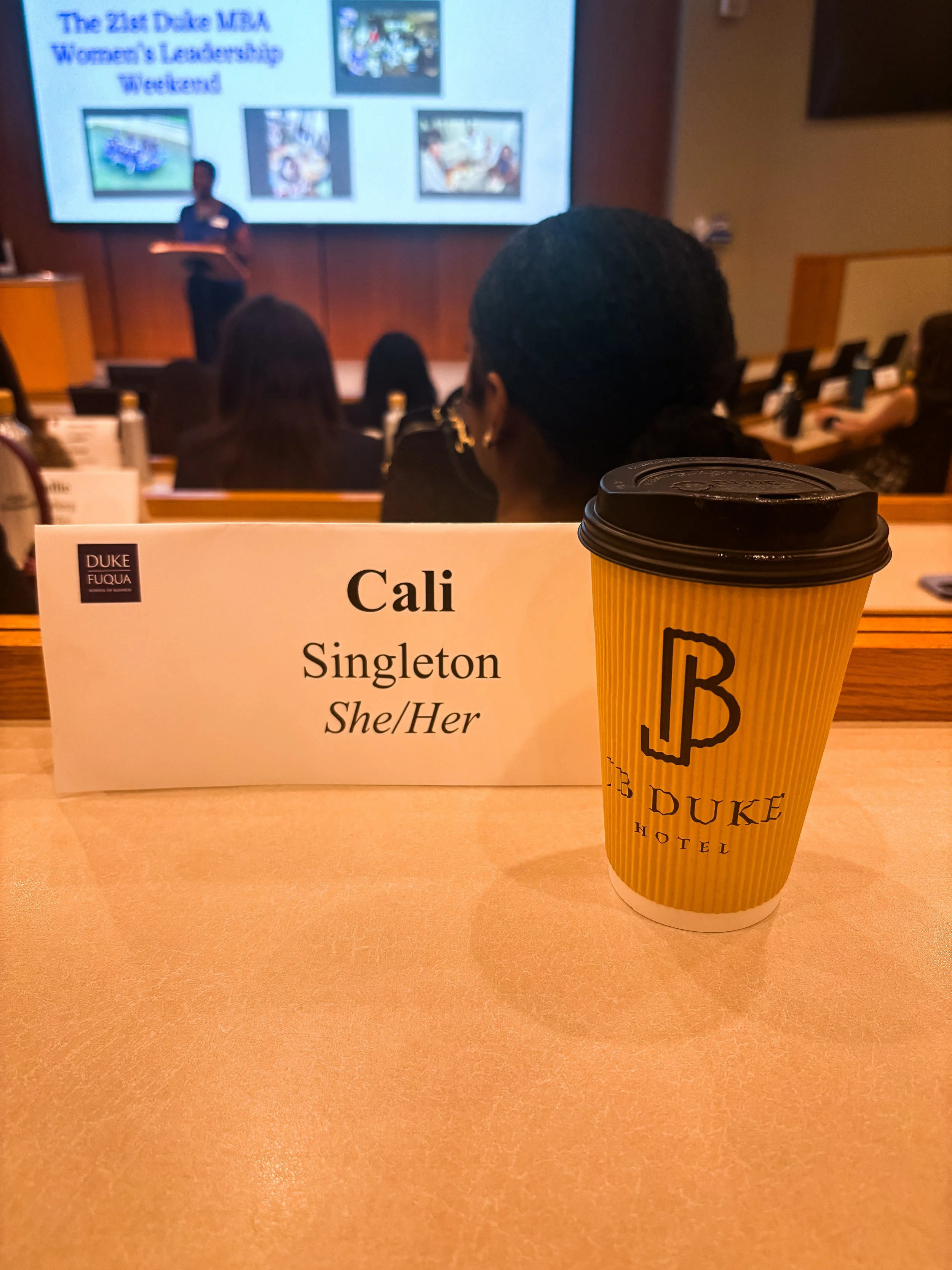 Conference name badge for Cali Singleton displayed on a seminar table with coffee and conference materials during a leadership event.