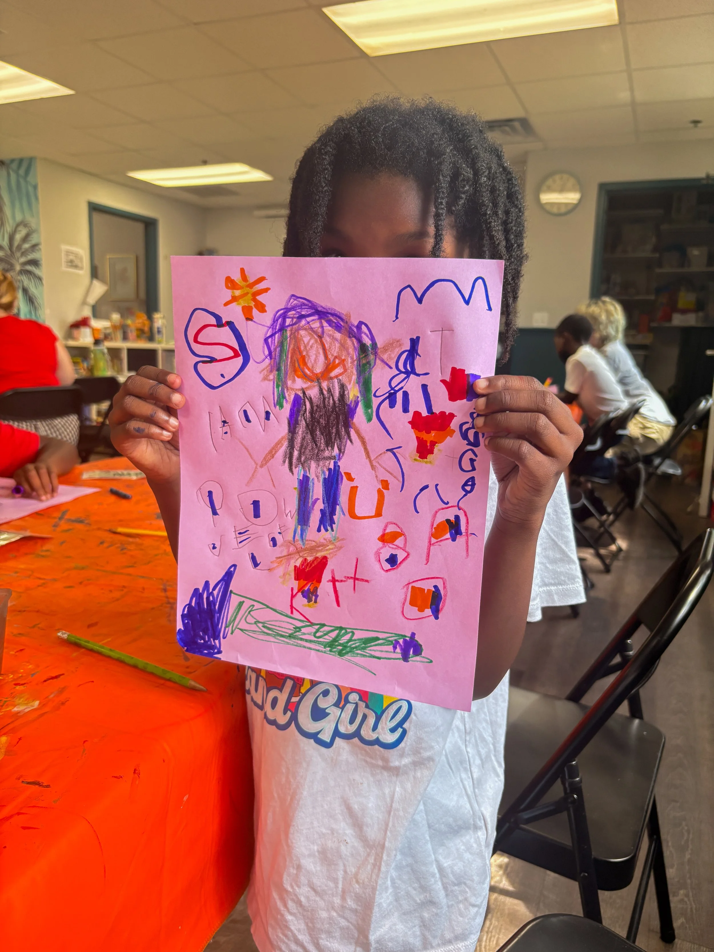 Child holding a colorful drawing during an art activity in a creative classroom environment.