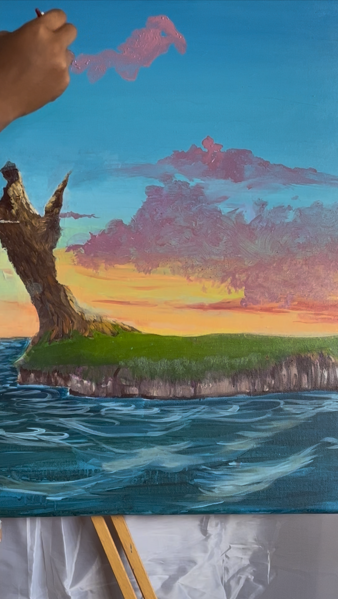 Painting of a landscape with a large tree on a small island, overlooking water, with a colorful sky at sunset or sunrise, and pink clouds.