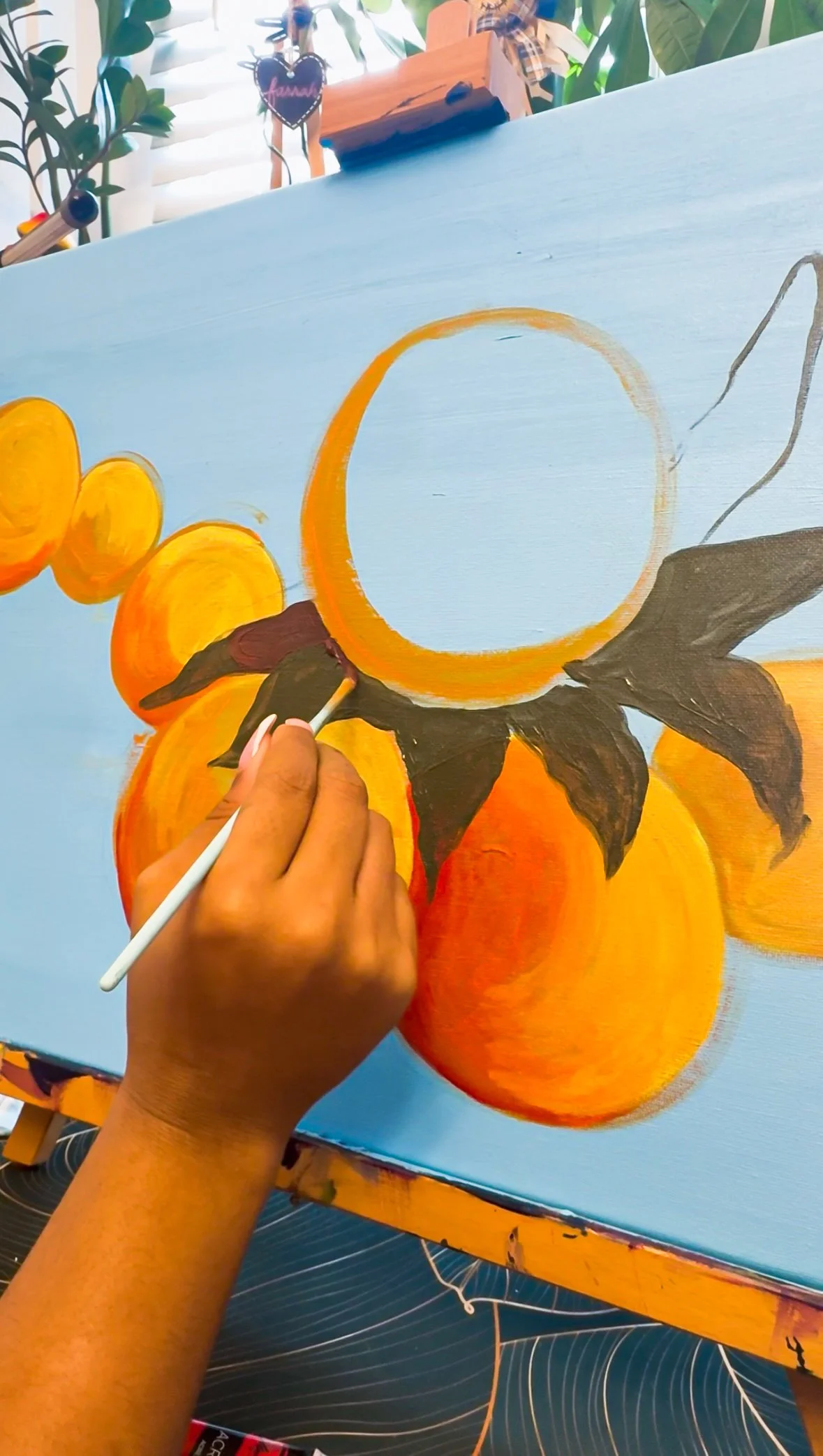 Artist painting a still life composition of oranges and a lemon on a canvas with a paintbrush in hand.