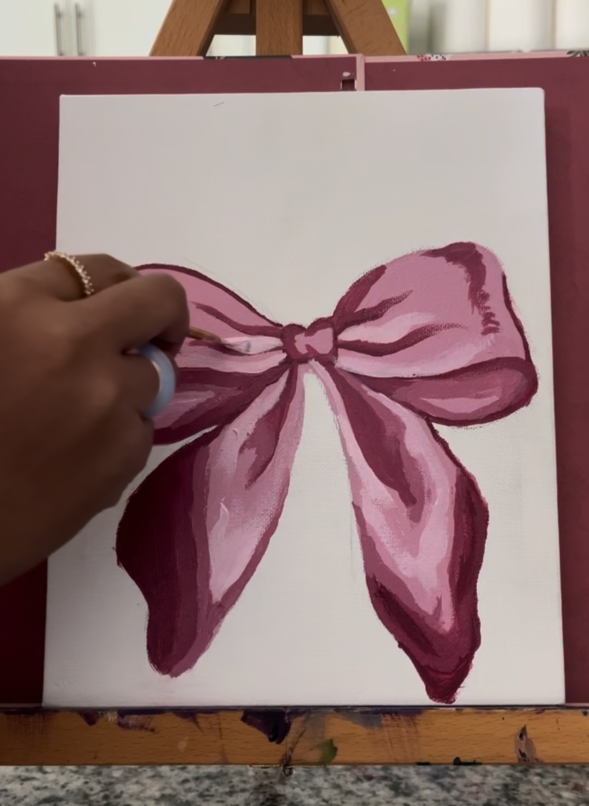 Person painting a pink bow on a white canvas.