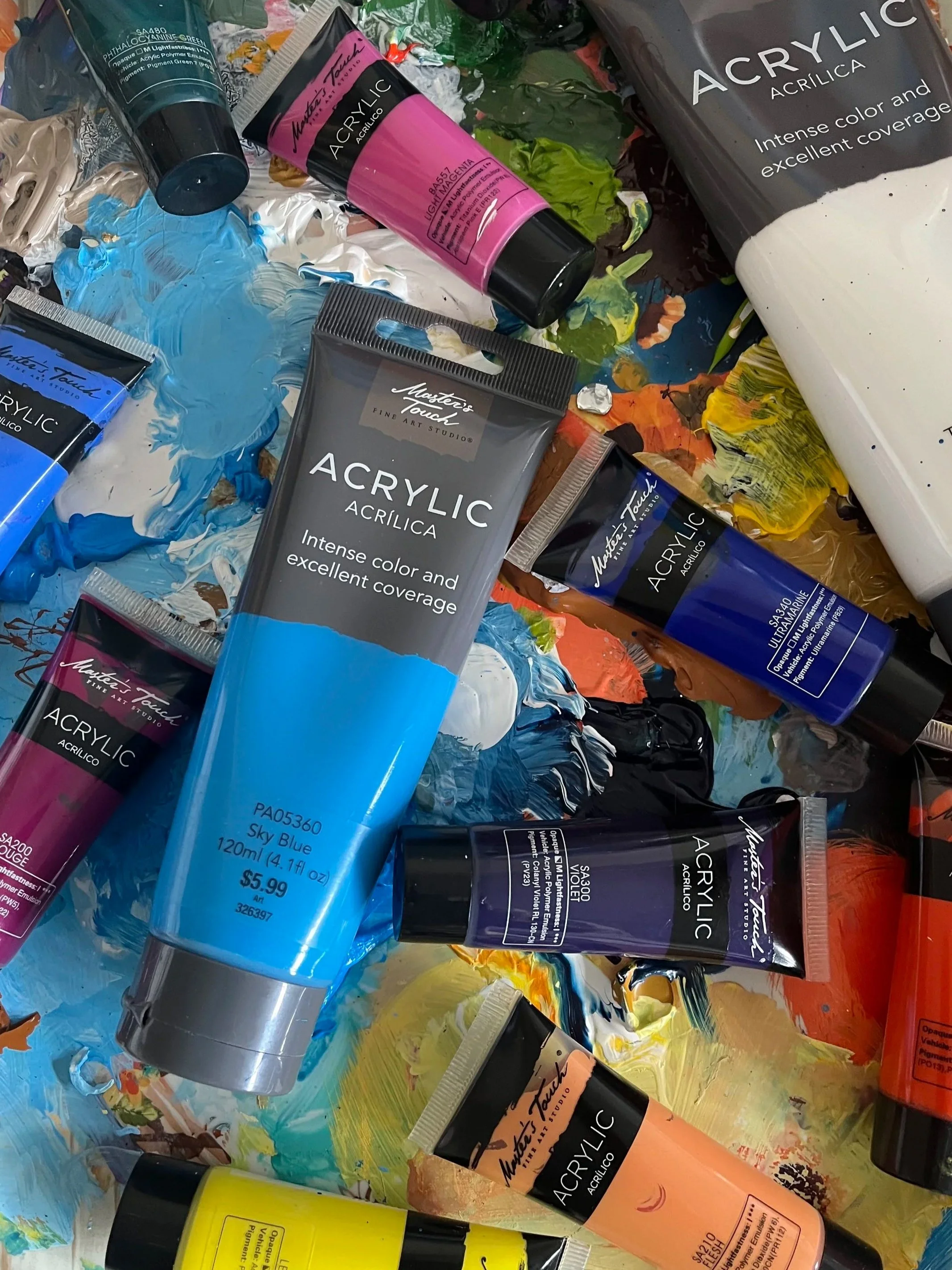 Assorted acrylic paint tubes in vibrant colors arranged on a paint-splattered surface.