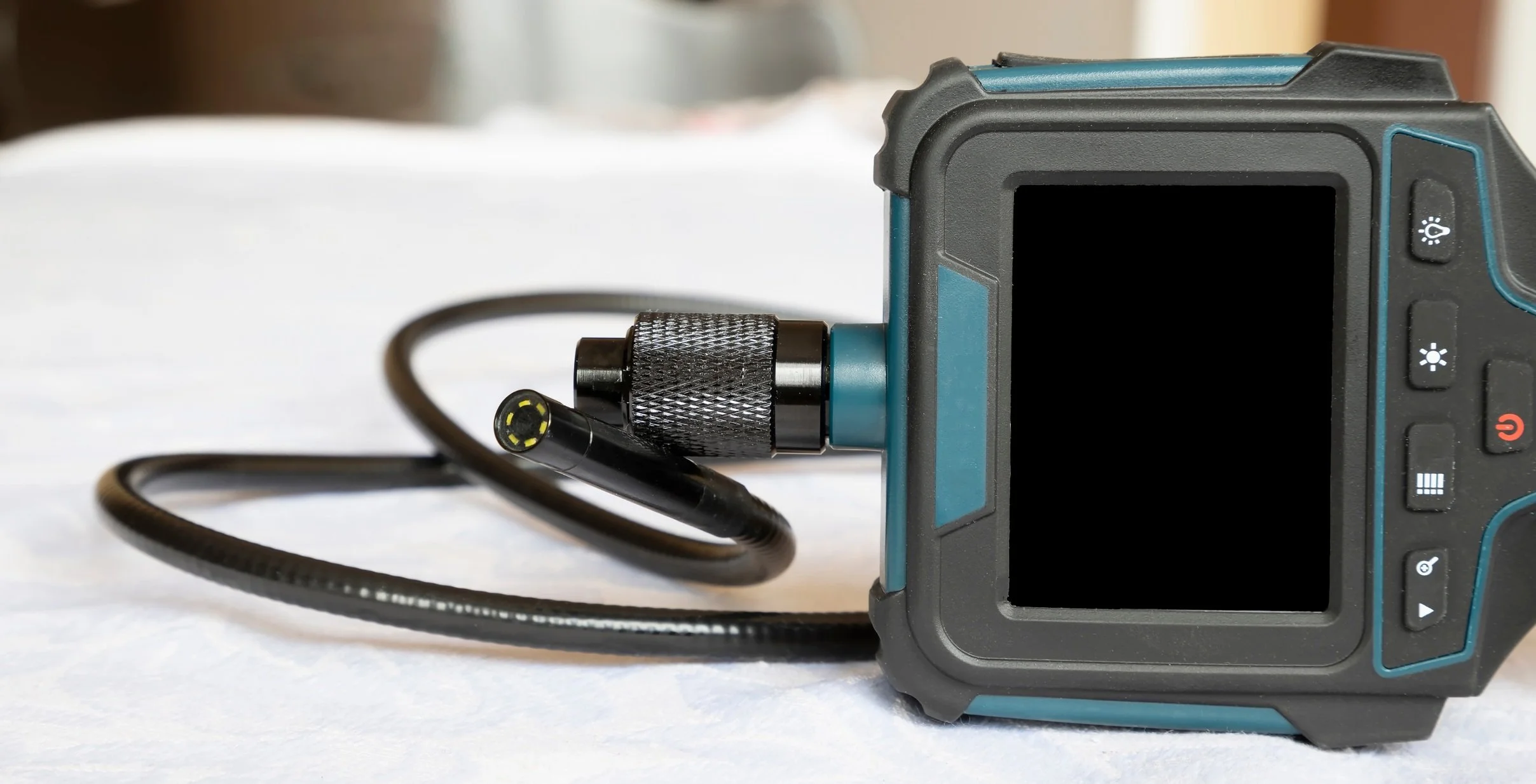 A digital camera with a thick black cable connected to its side, resting on a white surface.