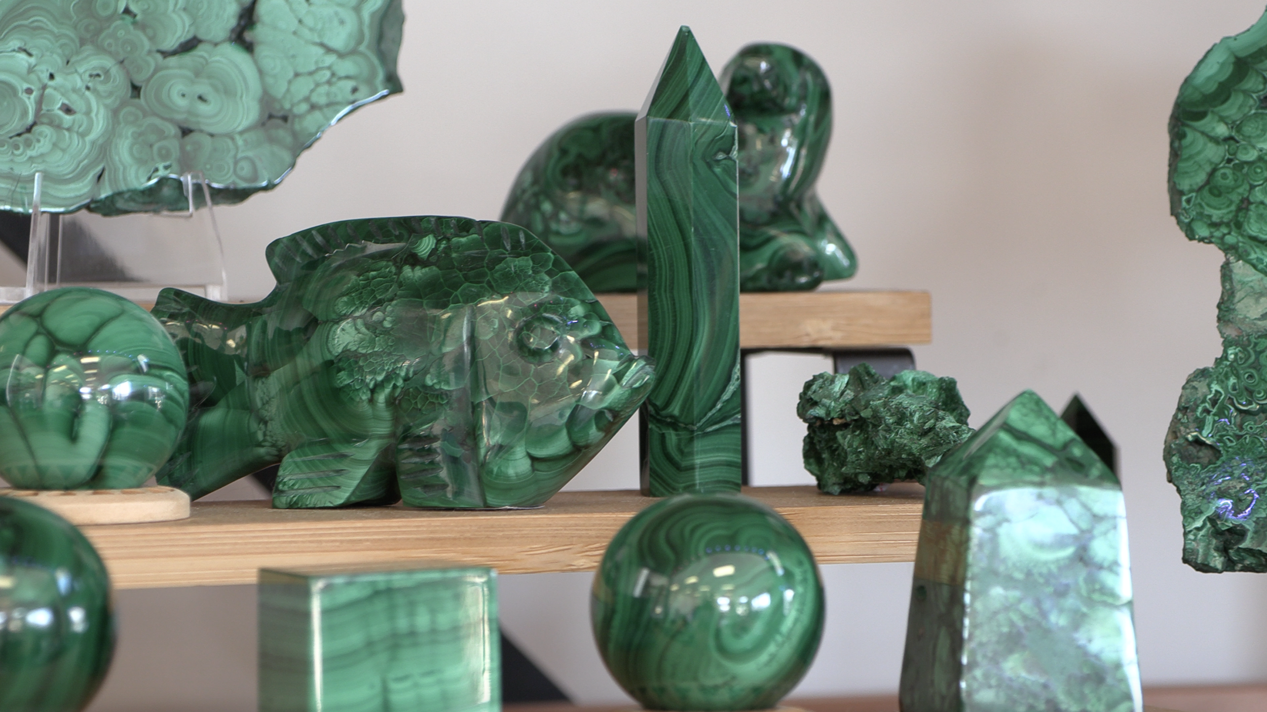 Collection of polished green malachite stones in various shapes on wooden shelves.