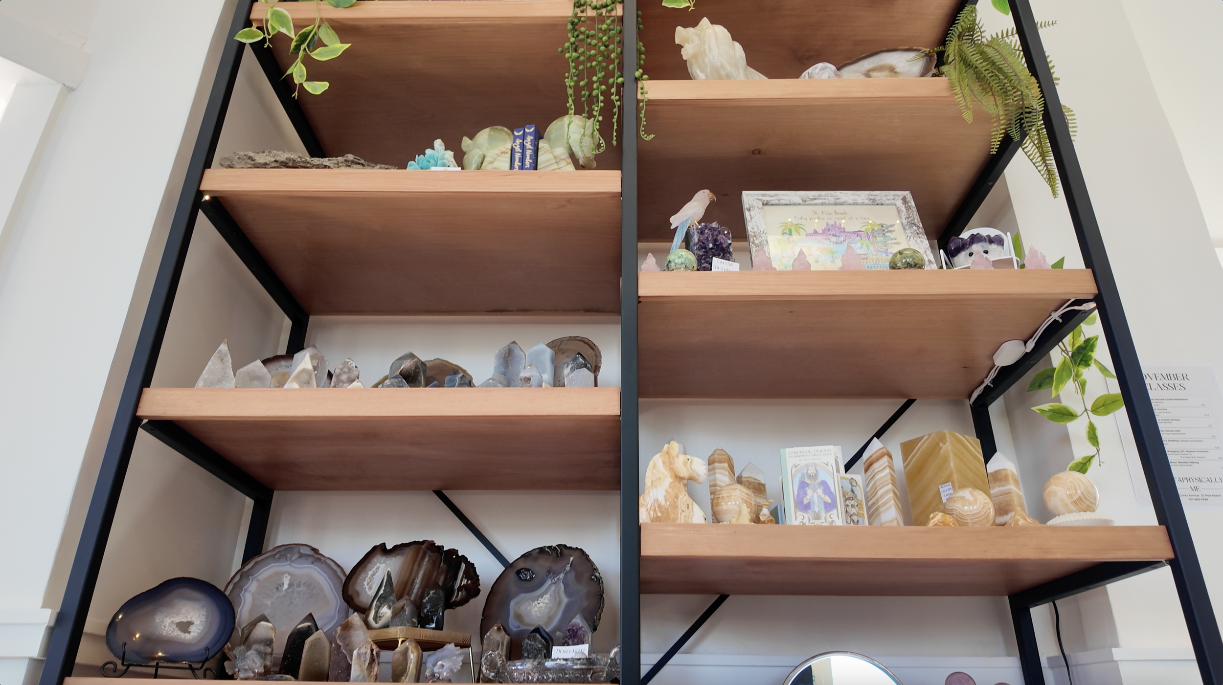 Wooden display shelf filled with various geodes, minerals, and crystals, with some decorative plants and a framed picture on the shelf.