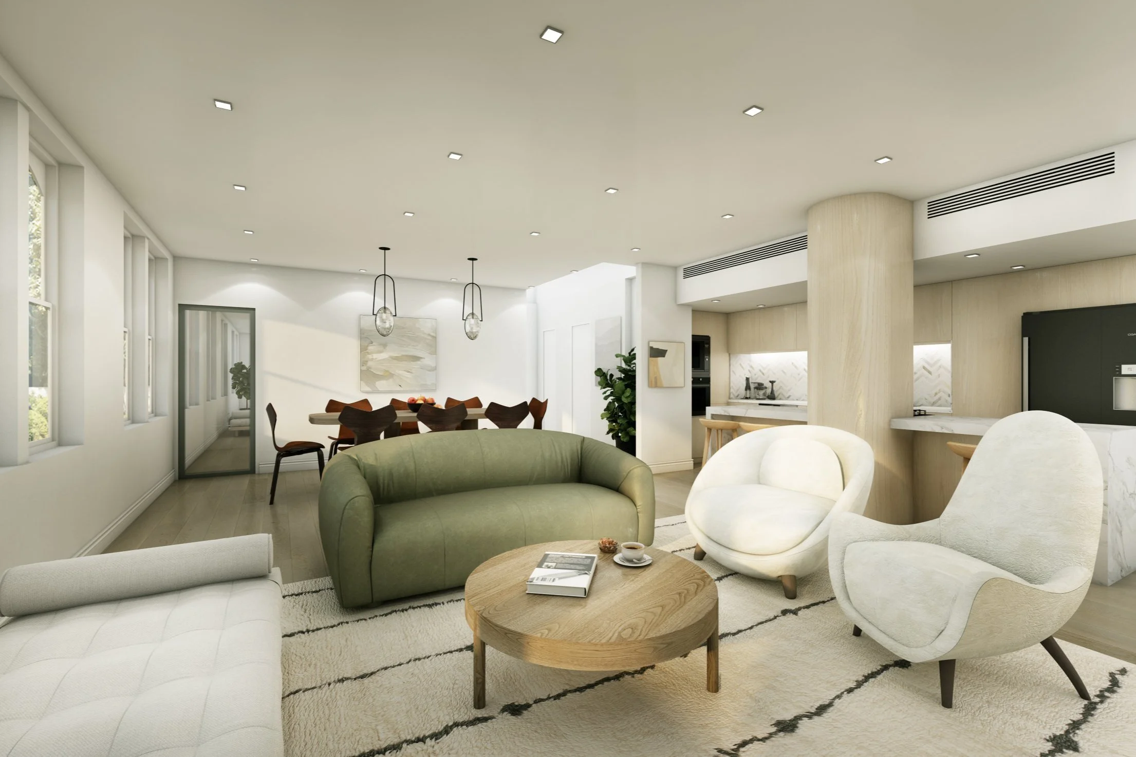 Modern living room with white walls, light wood flooring, multiple windows, a green sofa, two white lounge chairs, a round wooden coffee table with books and a cup, a dining area with a wooden table and chairs, and a kitchen with white cabinets and a