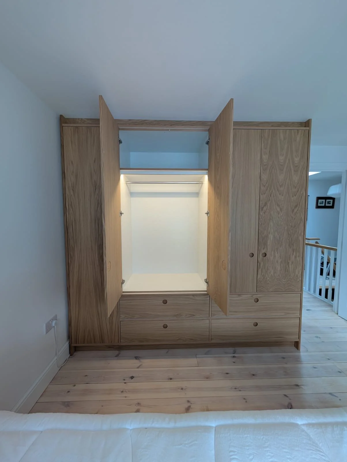 Open wooden wardrobe with drawers inside, situated in a room with light hardwood flooring.