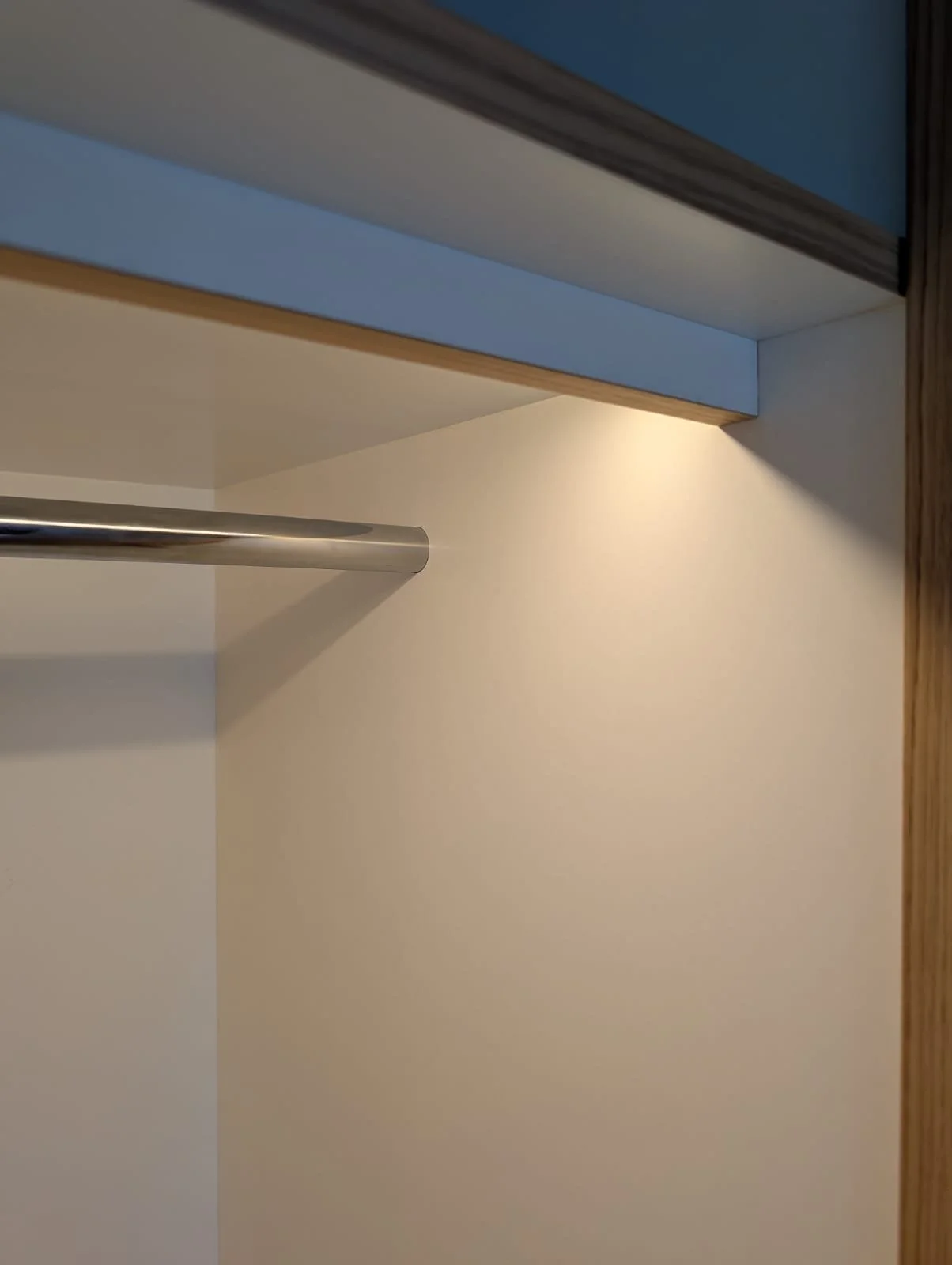 Close-up of the interior of an empty closet with a metal clothing rod, a beige wall, and a wooden panel.