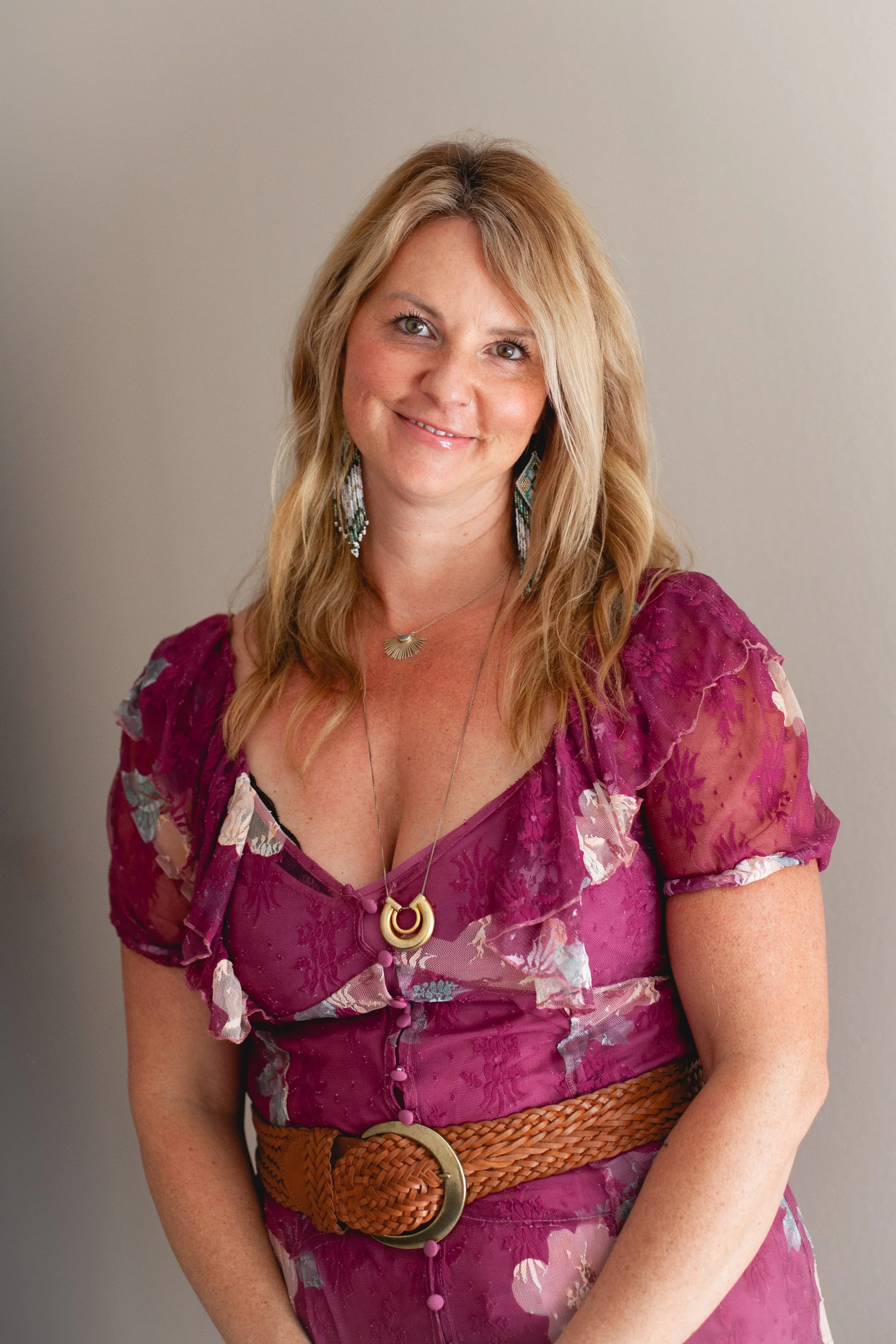 Modern house with wooden and white exterior walls, large glass window, surrounded by grassy field with mountains in the background.