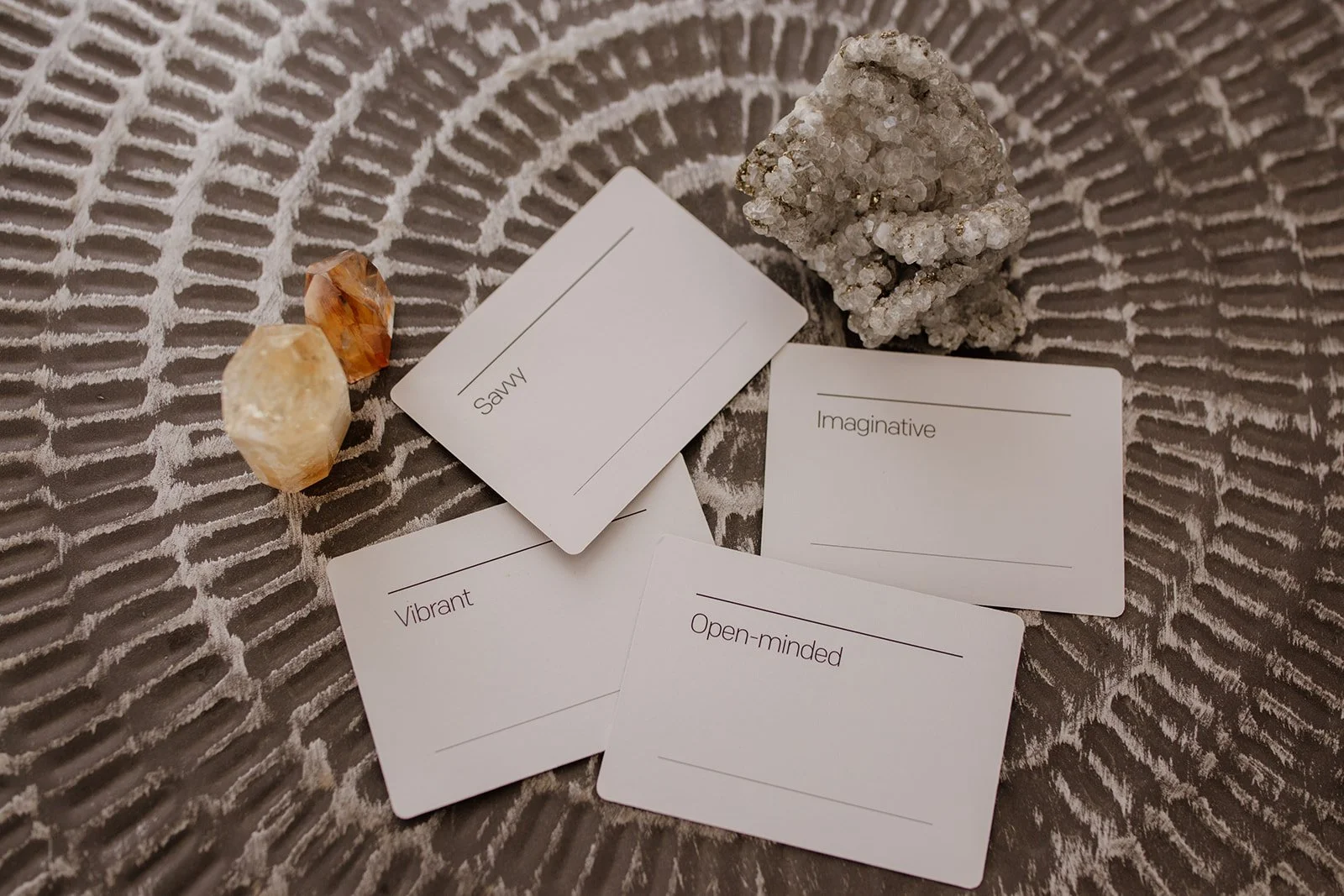 Four white cards with positive personality words and blank lines in a circular arrangement, surrounded by two crystals on a textured gray background.