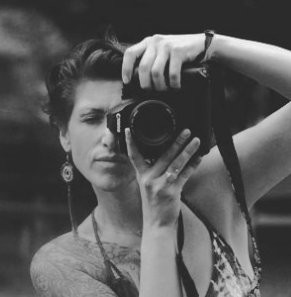 Black and white photo of a woman taking a selfie with a camera, looking at the camera lens.