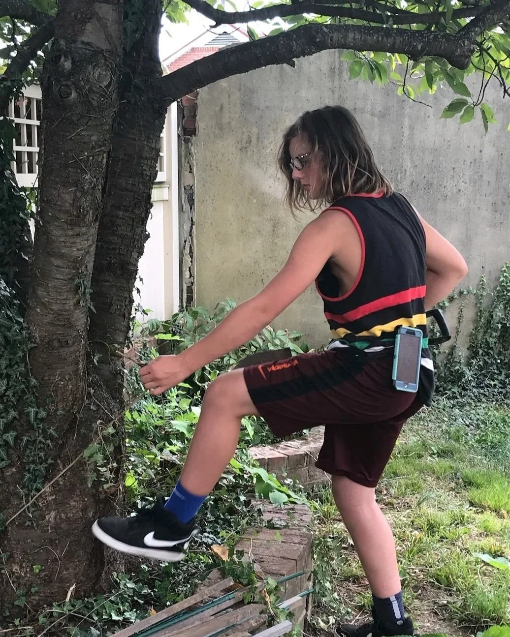 A teen independently clearing vines from a tree in a backyard.