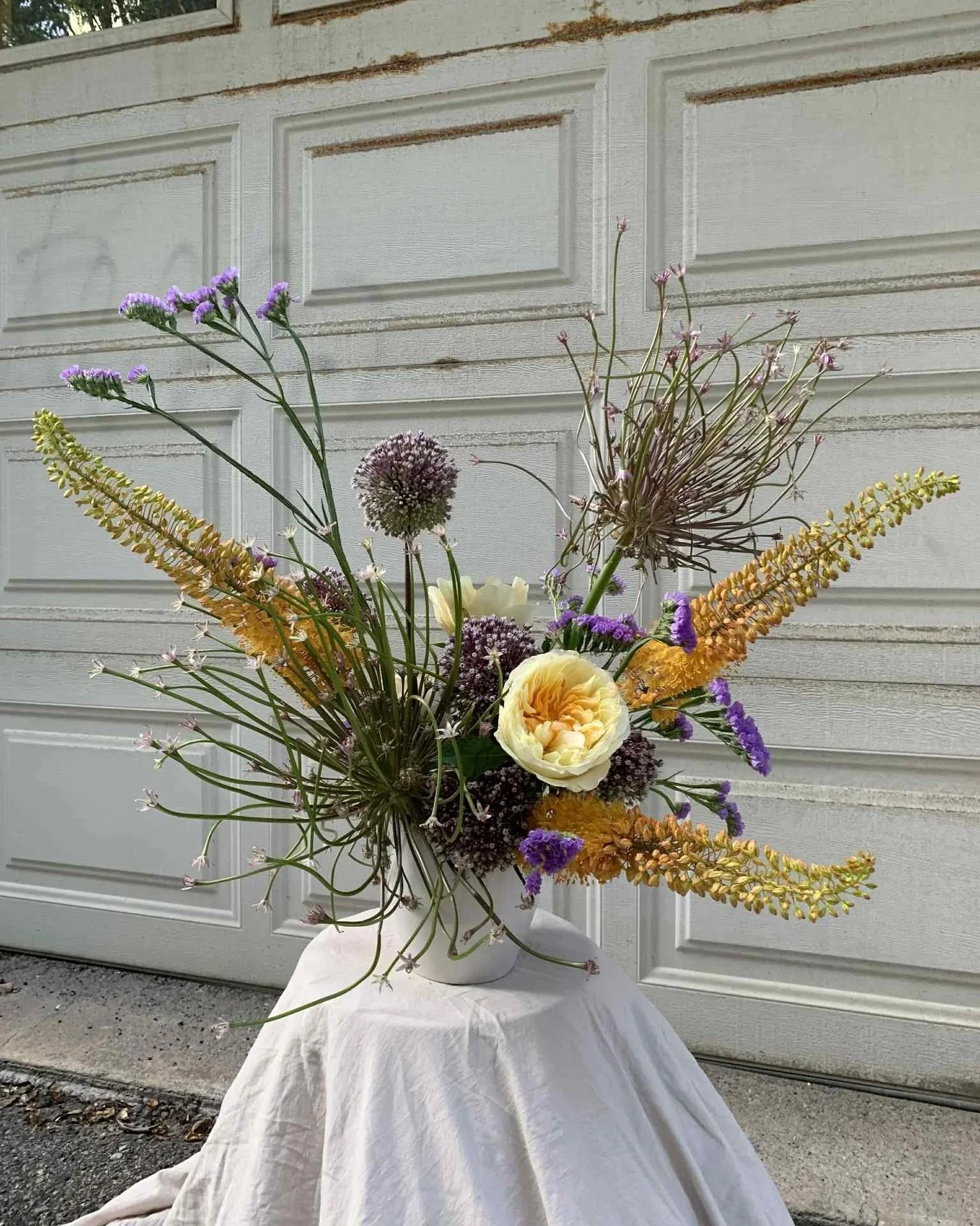 A floral arrangement with various flowers including large alliums, eremures, and yellow garden roses.