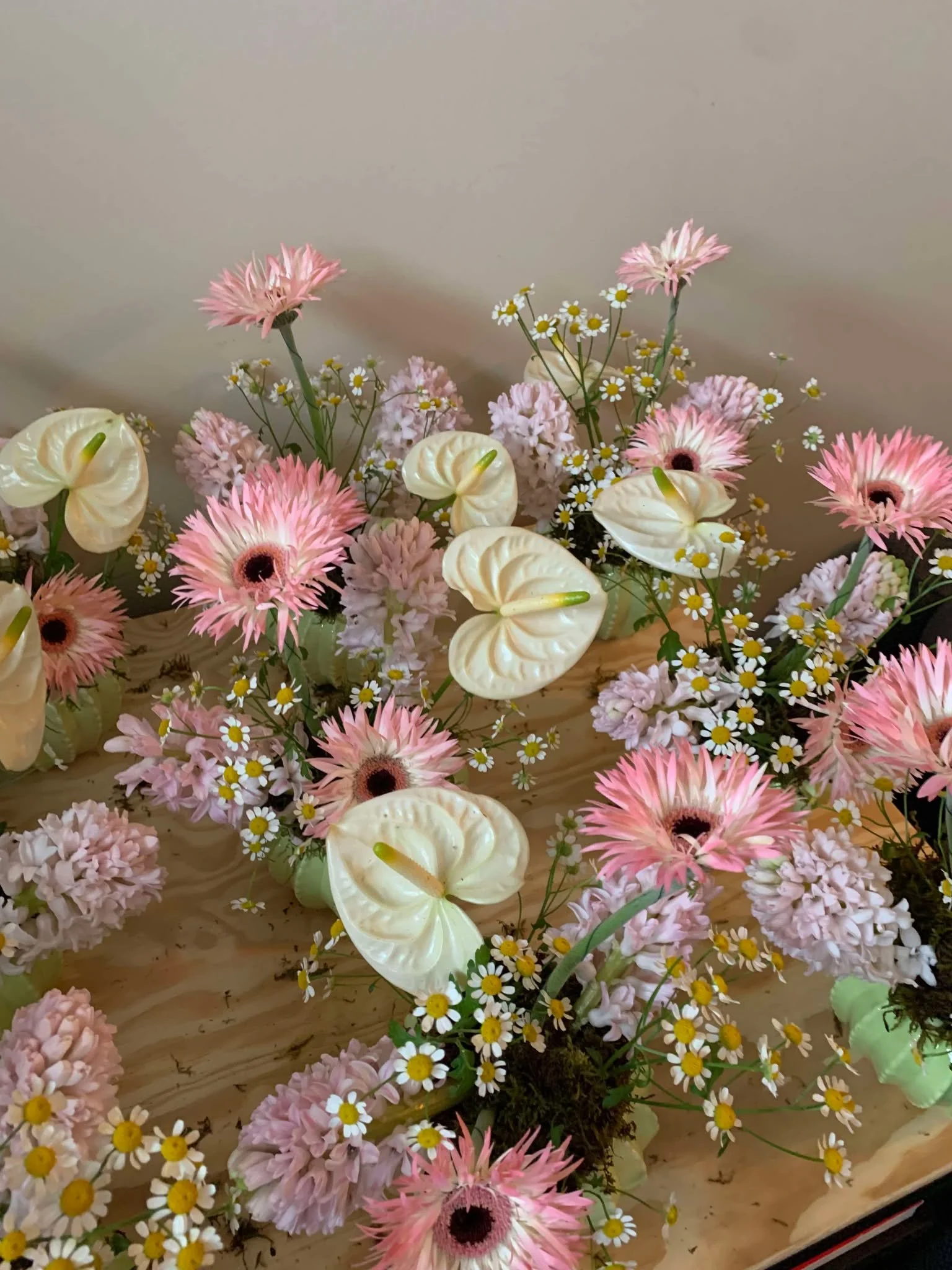 An arrangement of pink spider daisies, white anthuriums, and pink hyacinth displayed on a light wooden surface.