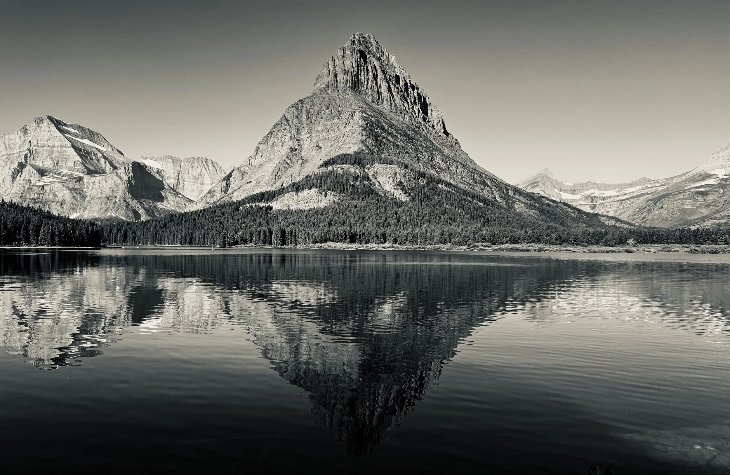 Black and white photo of a mountain with a sharp peak, reflected in a calm lake.