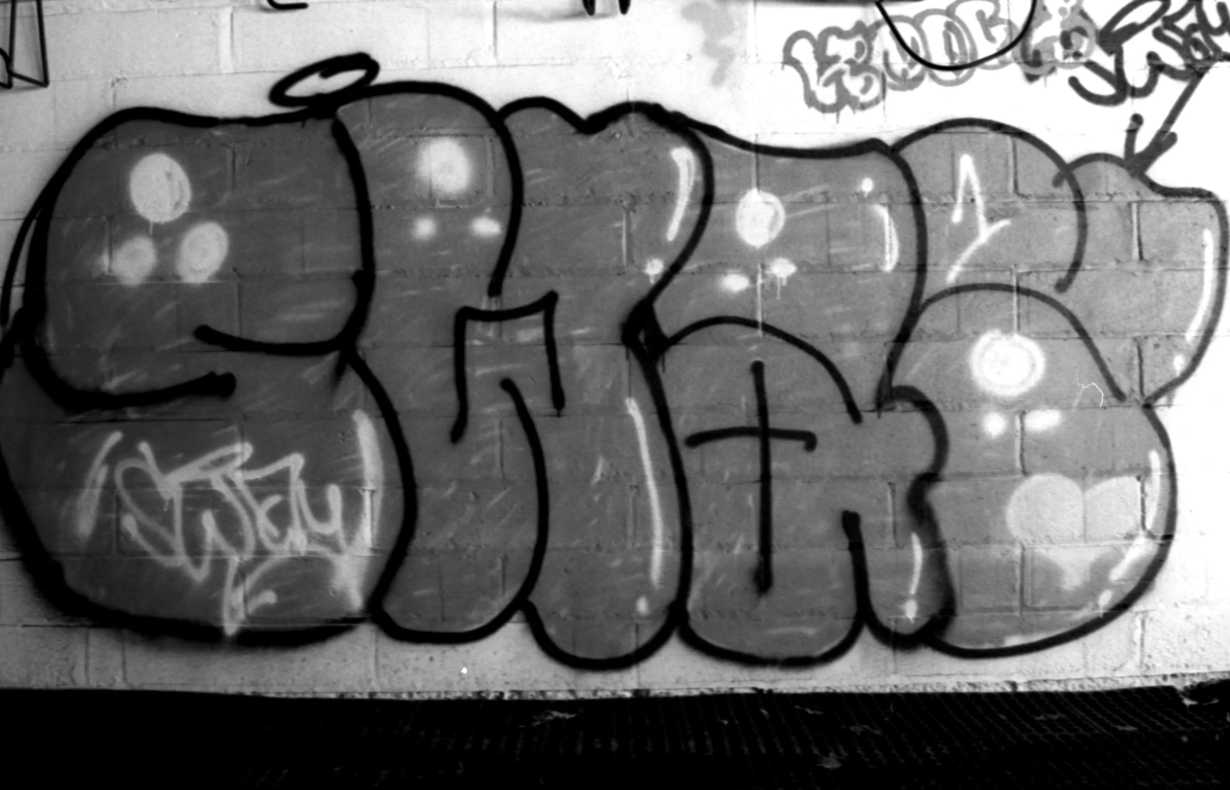 Black and white graffiti art on a brick wall with bubble letters and highlights.