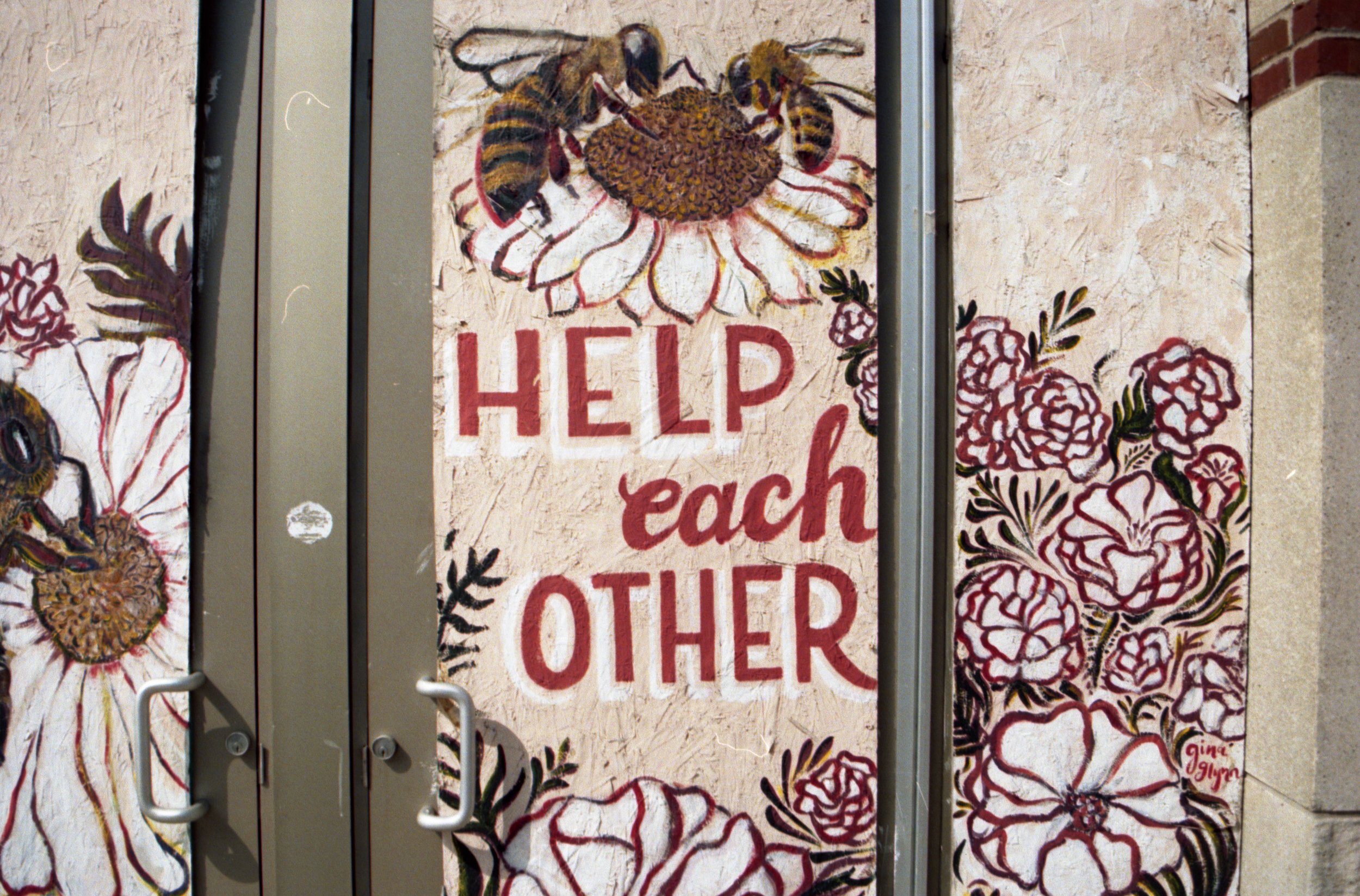 Door with painted floral designs and a sign that reads 'Help each other'.