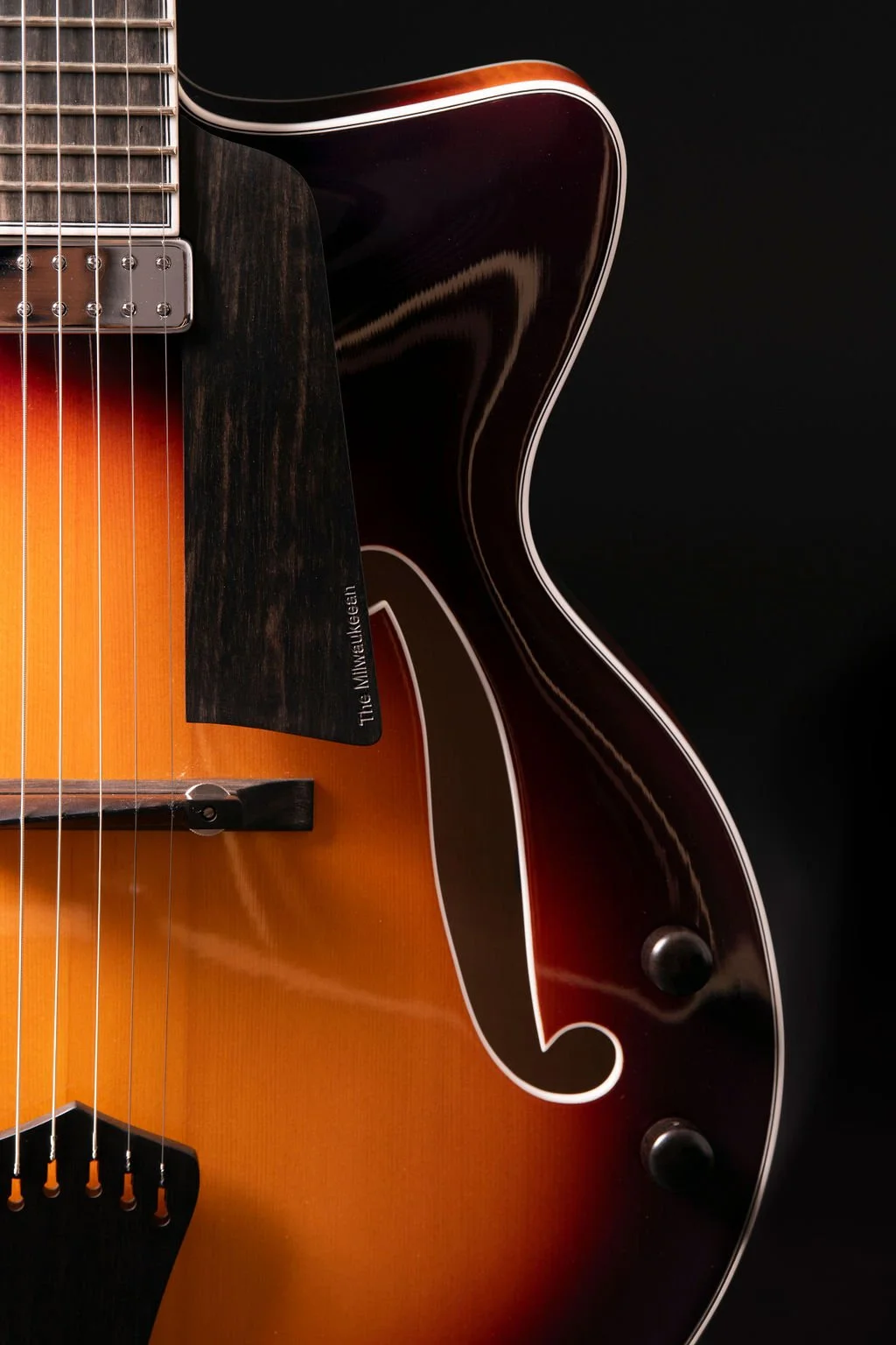 Closeup view of a guitar’s F-holes with pickguard engraved with “The Milwaukeean”