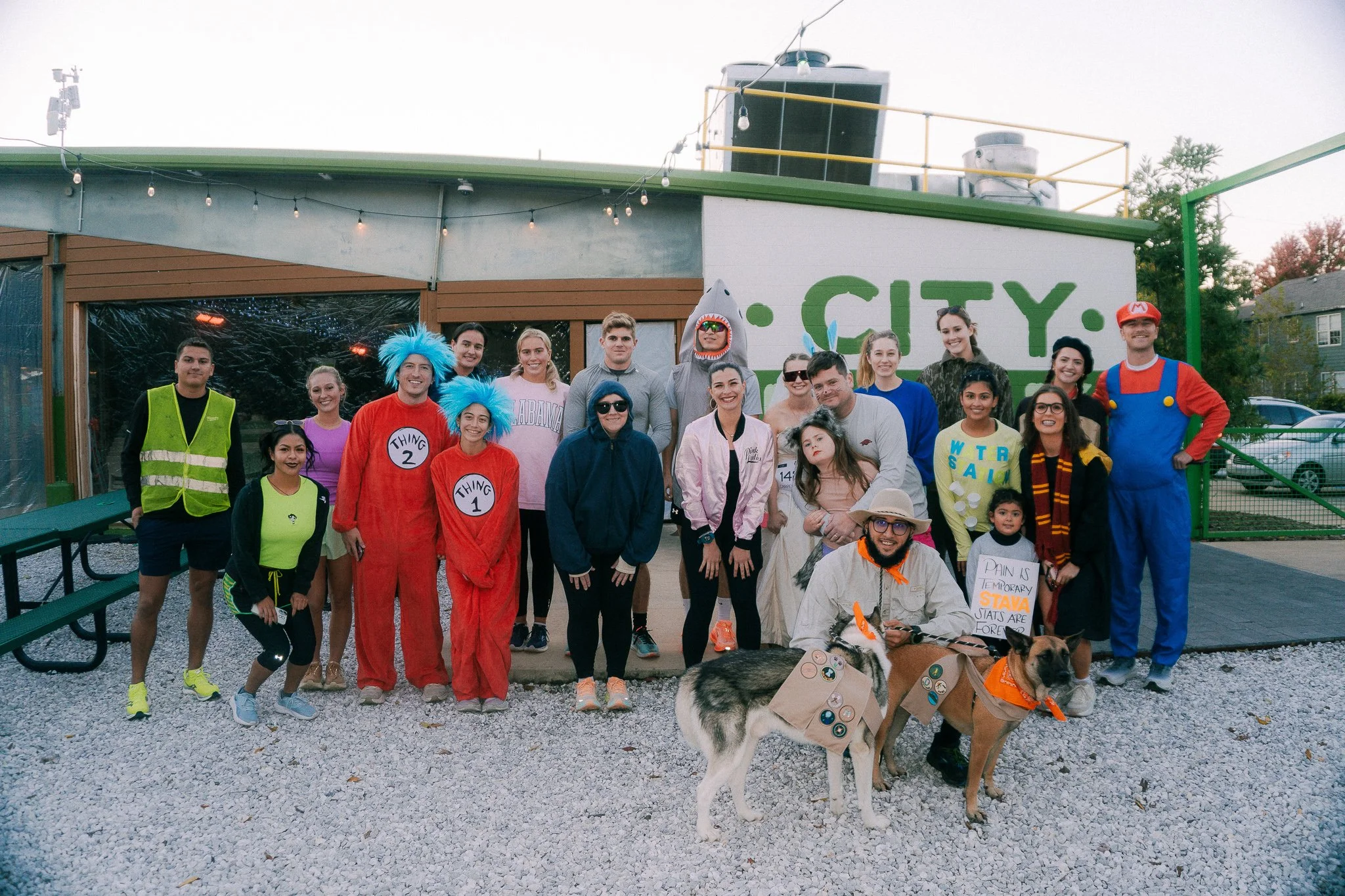 A large group of people in costumes and casual TimberTrout apparel gathered outdoors with two dogs.