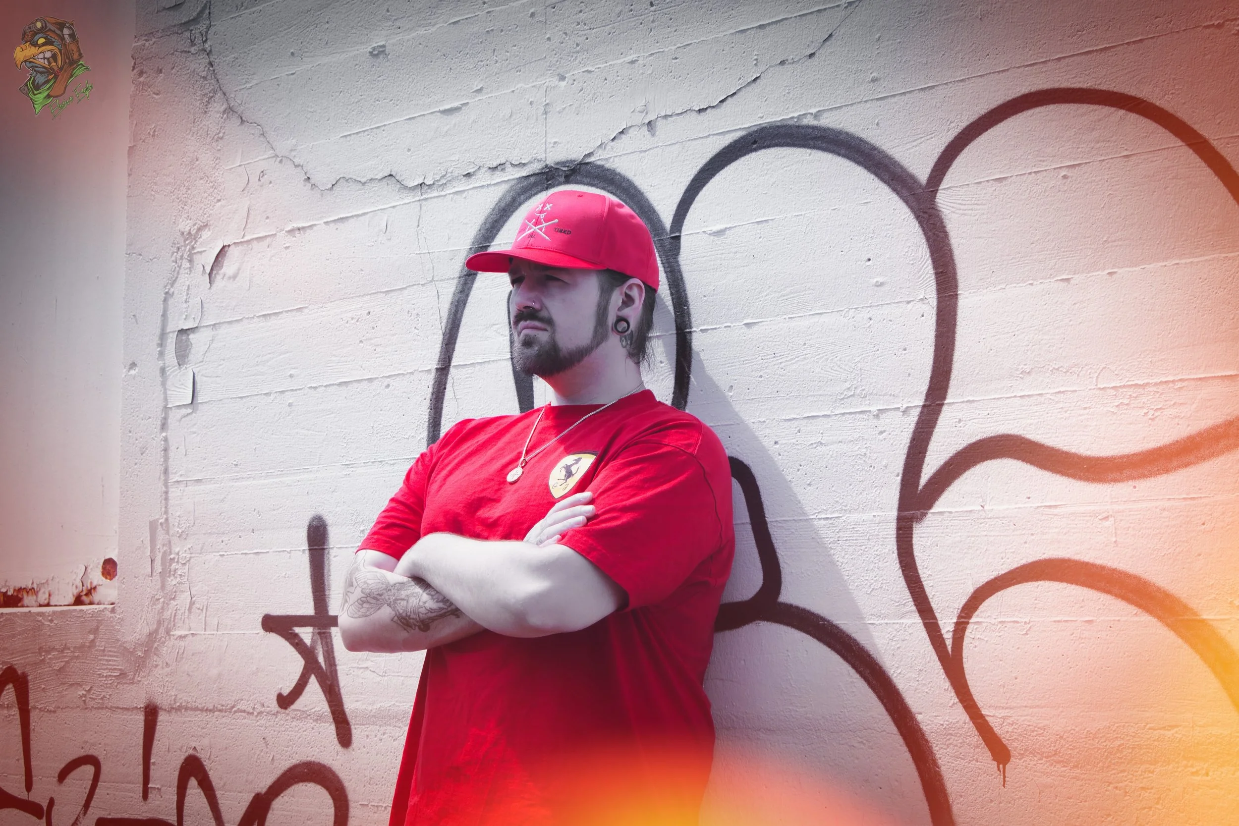Man in red clothing and cap leaning against graffiti wall.