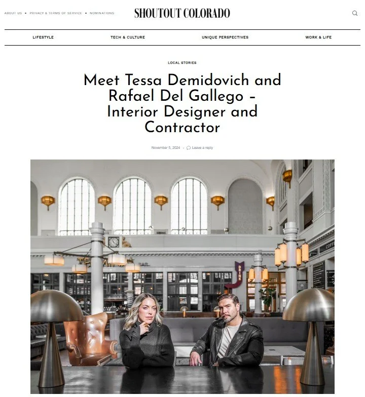 Photograph of a man and woman sitting at a dark table in a stylish cafe or restaurant with high arched windows and modern decor. The woman has blonde hair and is wearing a black sweater, and the man has short hair and is wearing a black leather jacket.