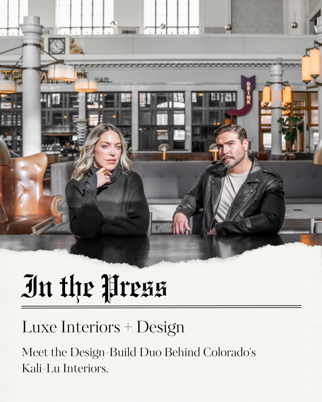 A man and woman sitting at a table in a stylish, modern interior space with warm lighting, leather armchair, and large windows in the background.