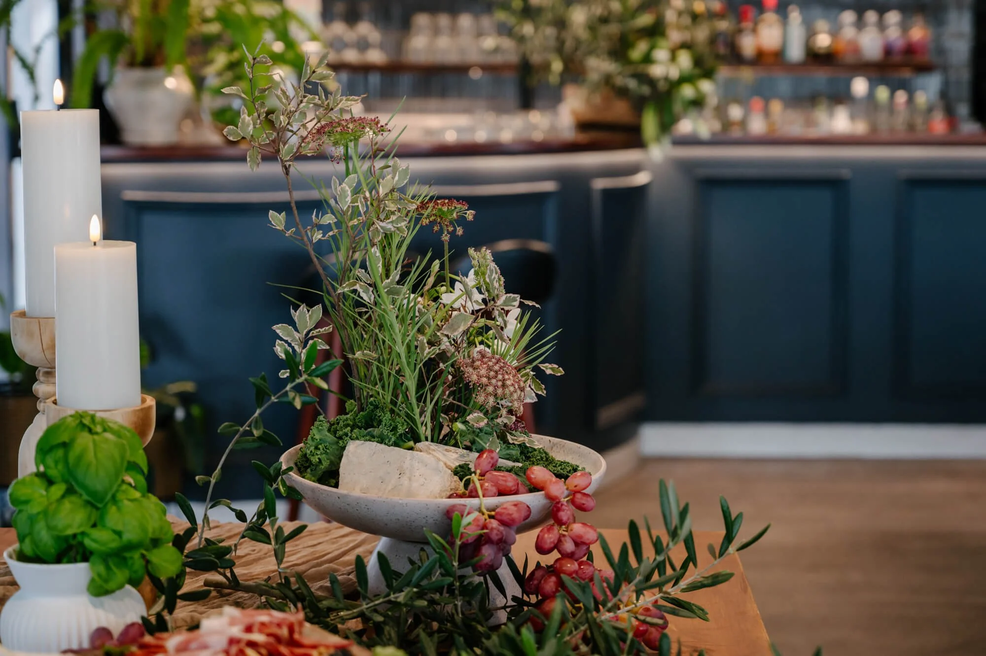 Interior of a home decorated with candles, plants, and pink grapes on a wooden table.