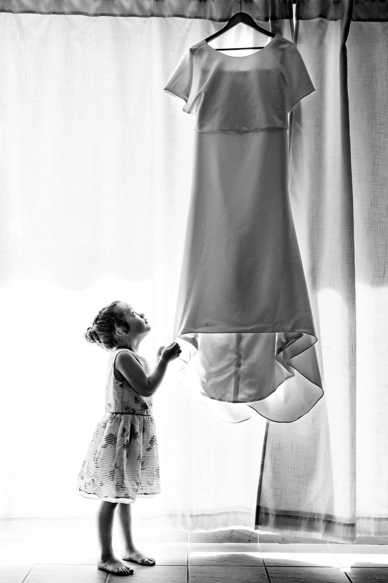 A young girl in a dress looking at a hanging wedding dress.