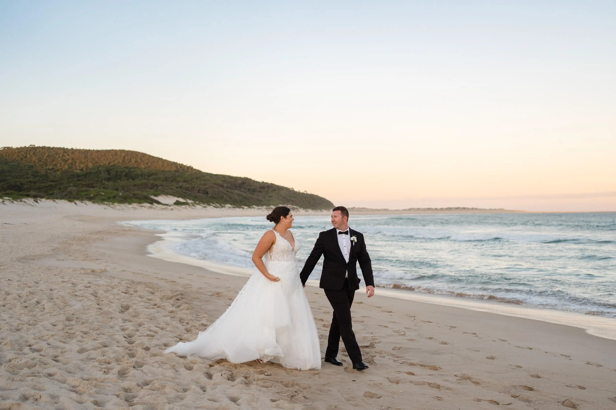 Bride and groom walking hand in hand on the beach at sunset