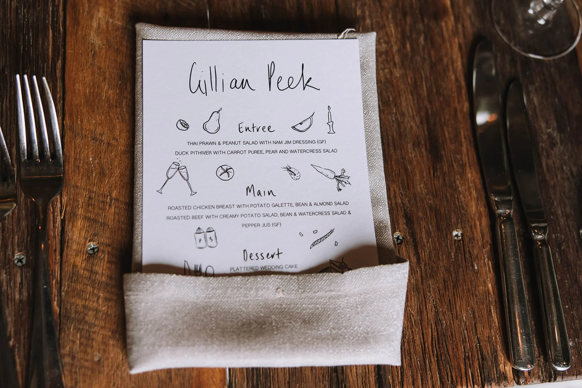 Restaurant menu on a table with a fork on the left, knife and spoon on the right, and a clear glass at the top right.