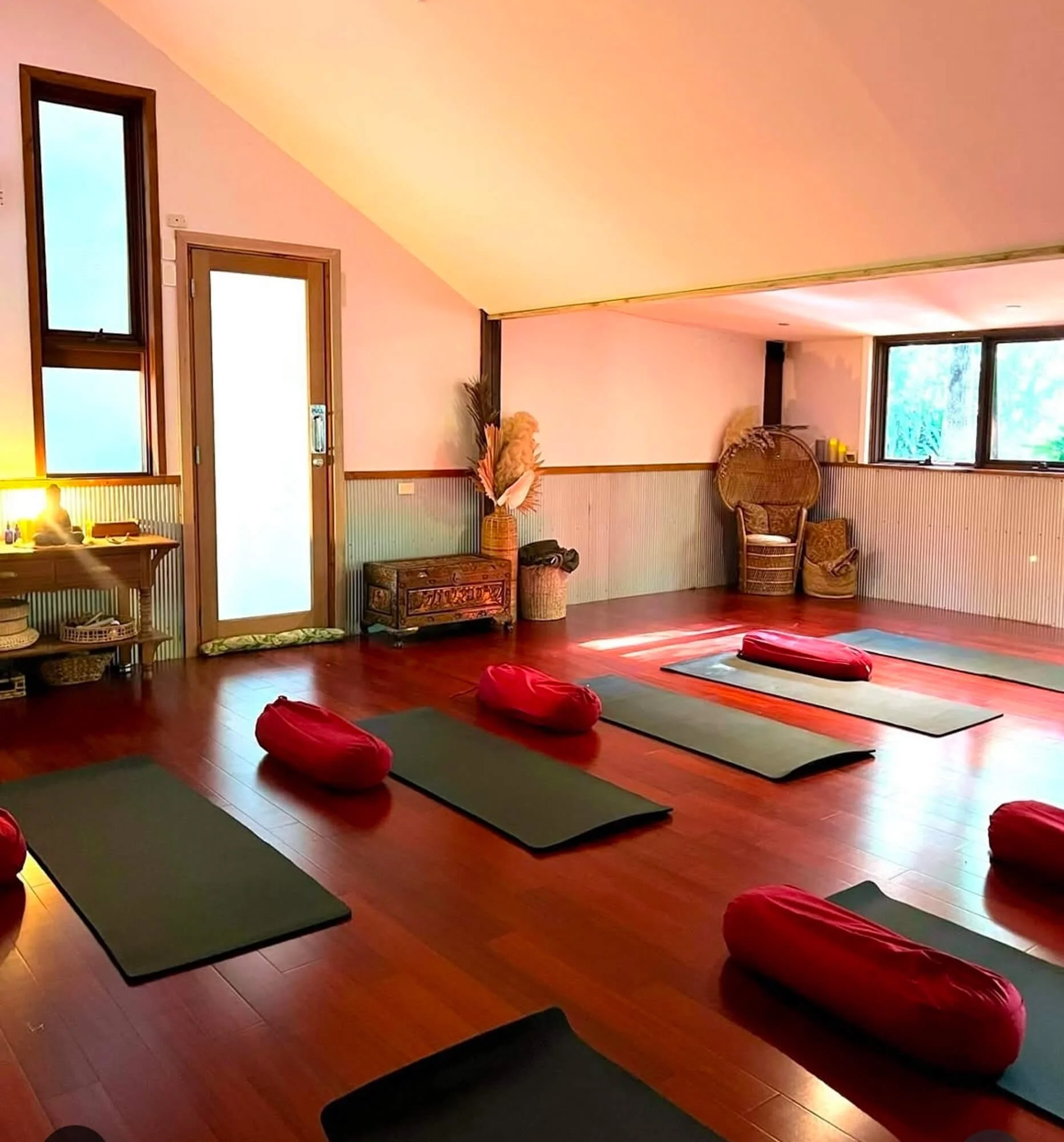 Yoga class setup with mats and bolsters in a well-lit studio with wooden floors and windows.