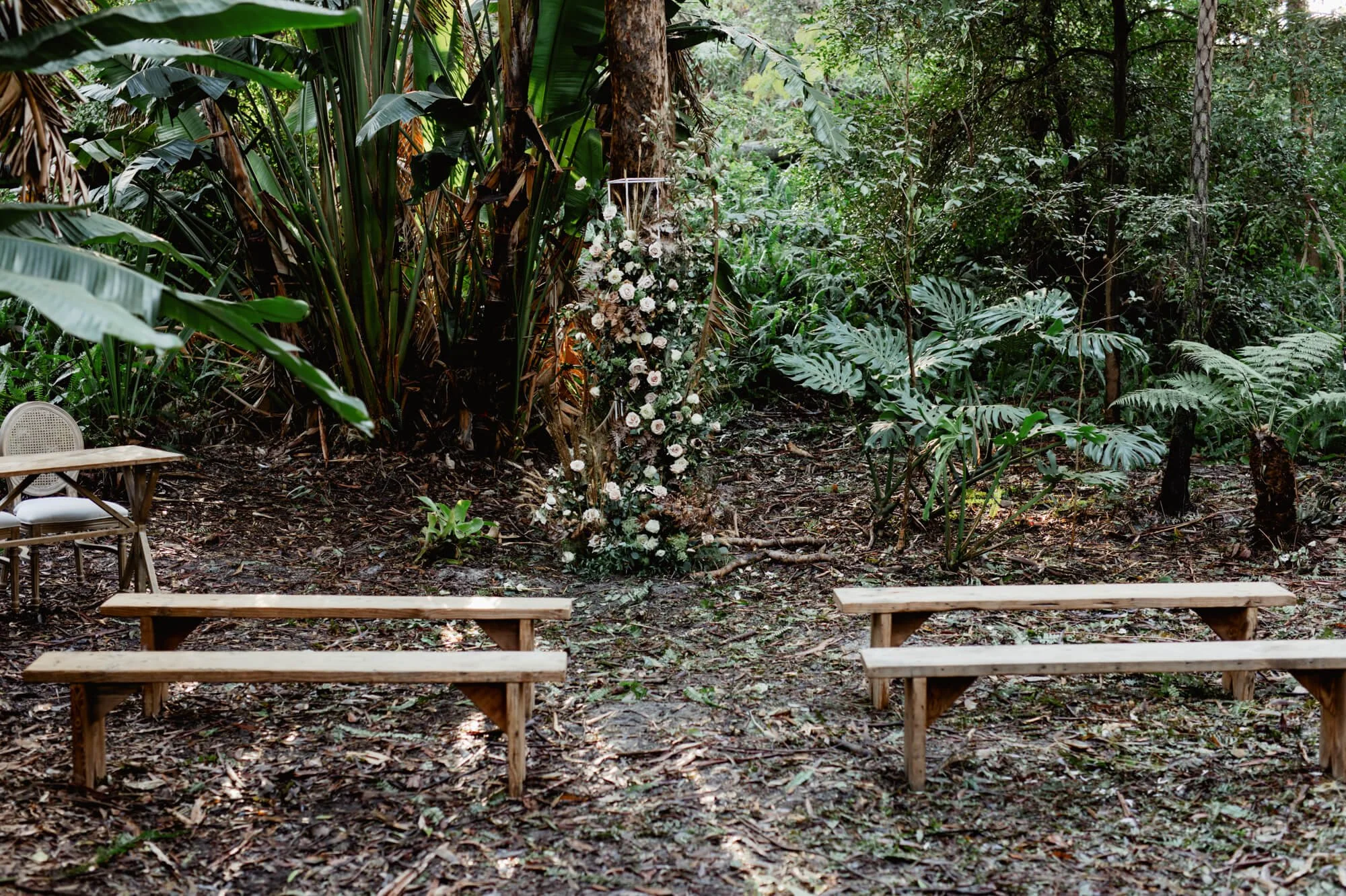 Outdoor wedding ceremony setup in a lush jungle with benches and a floral arch.