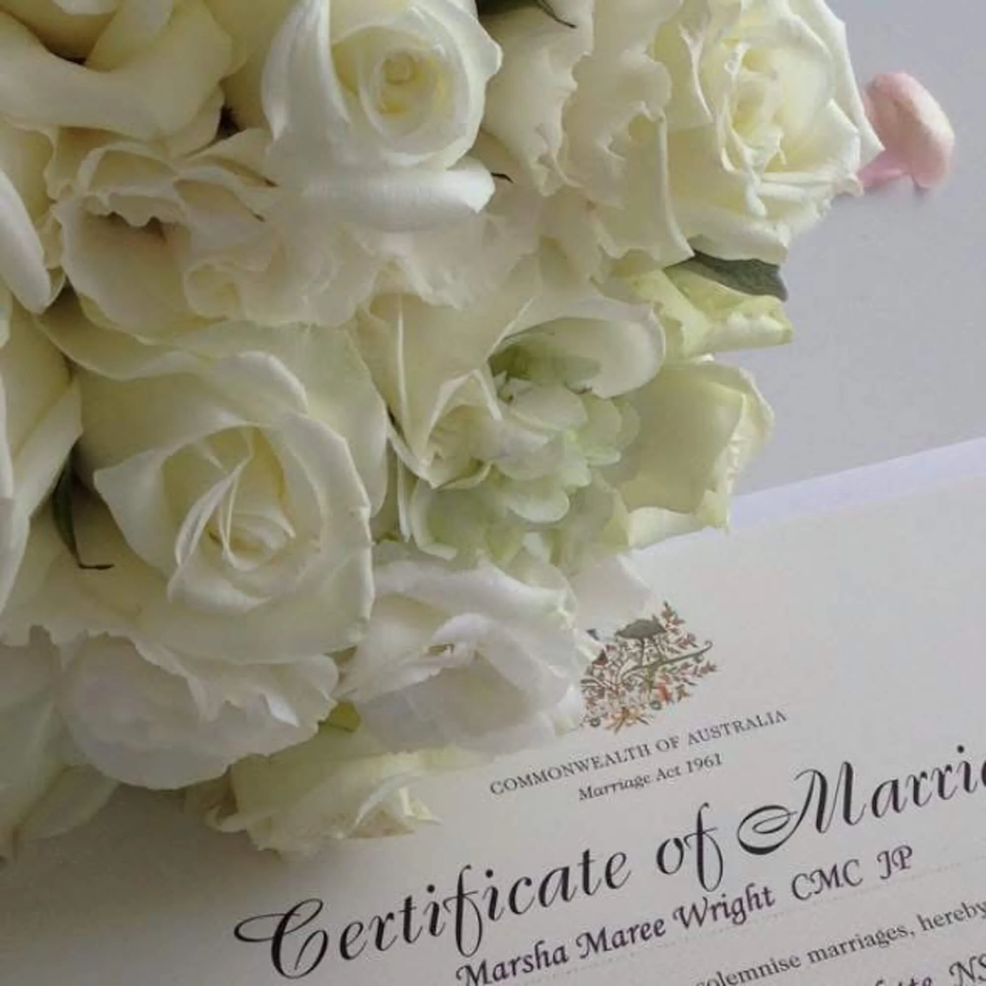 A bouquet of white roses resting on a marriage certificate from the Commonwealth of Australia.