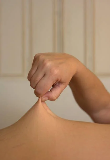 Close-up of a hand pinching the skin on the shoulder in front of a beige door.