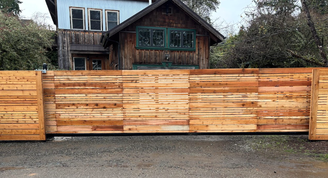 New wooden fence in front of a rustic home with dark brown and teal accents.