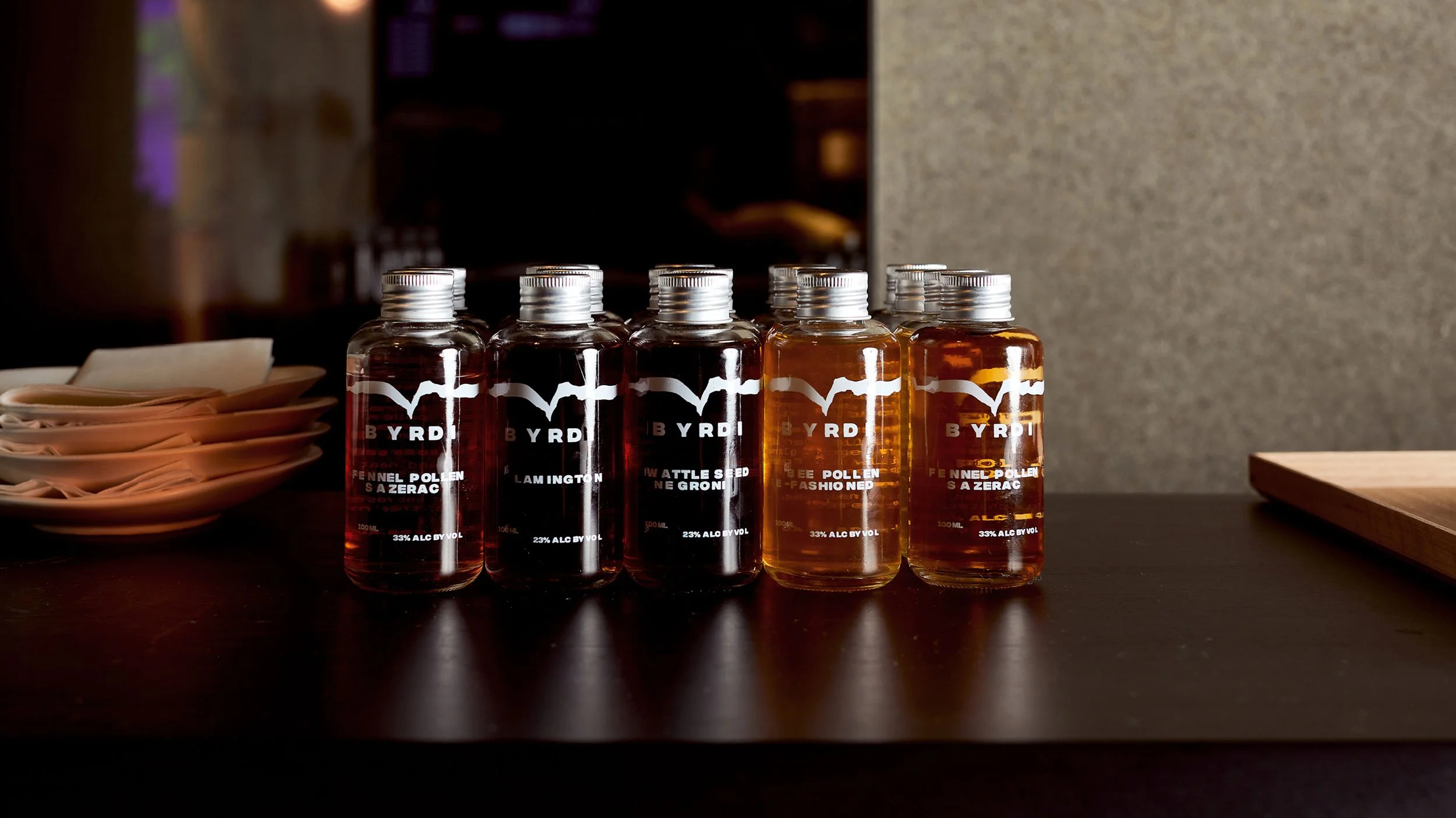Collection of five Byrdi mini bottled cocktails displayed on a wooden surface in shades of red and orange.