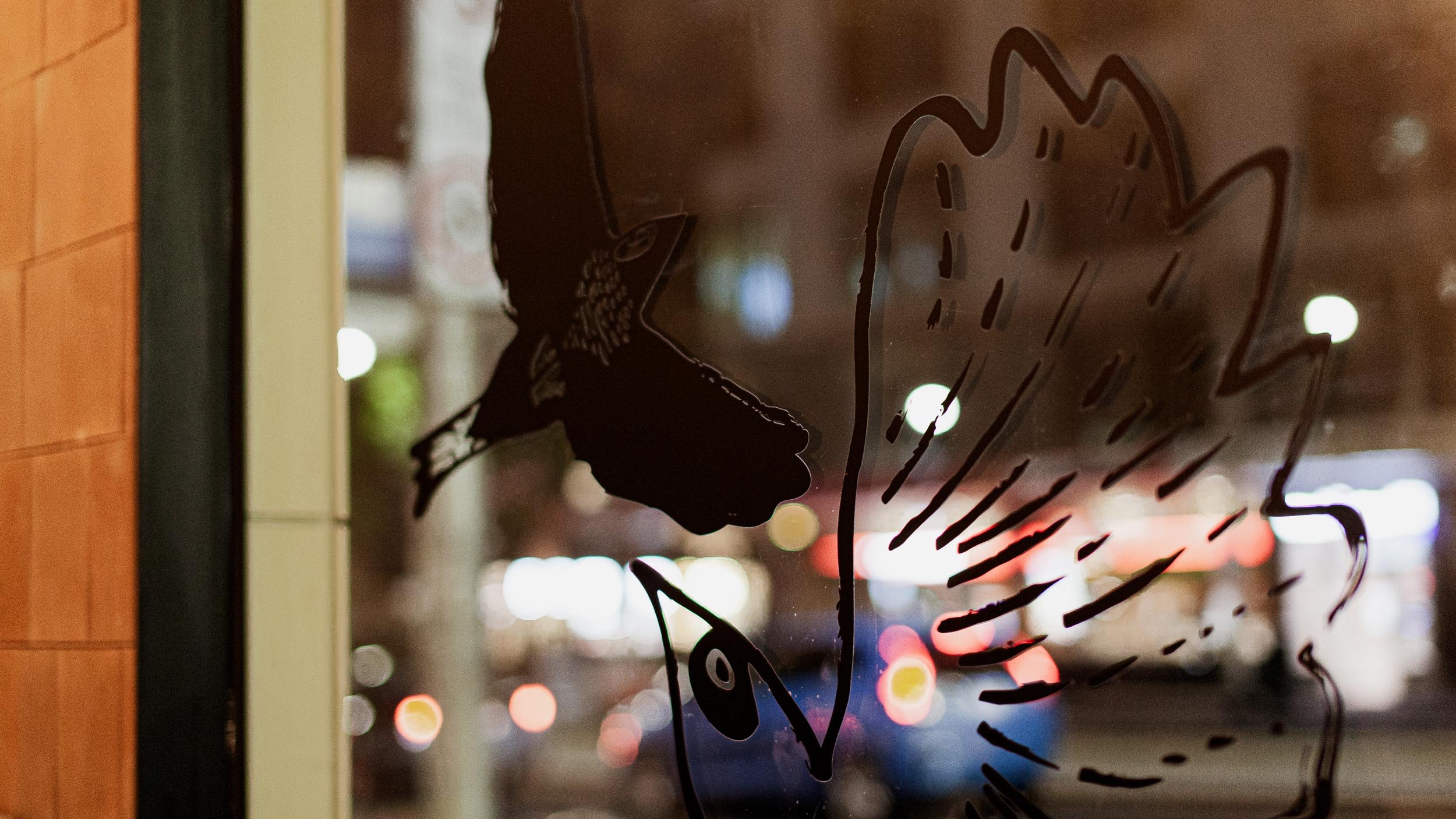 Closeup of two bird illustrations as a black decal on the Byrdi window. Birds are drawn loosely with lines and dots.