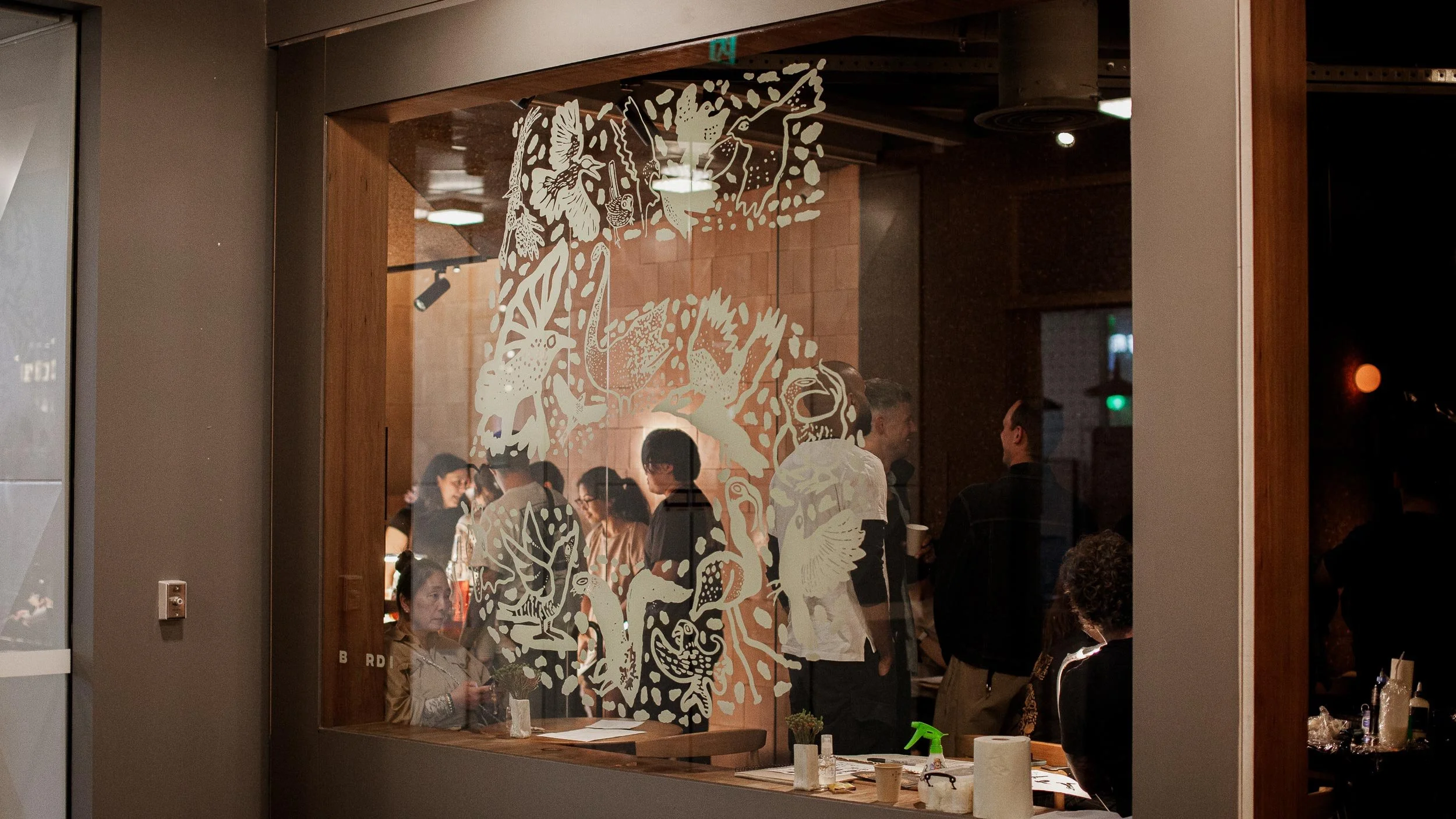 Illustrated birds in a 5 shape applied as a decal on the Byrdi window for their 5th birthday. We can see lots of people inside Byrdi through the window.