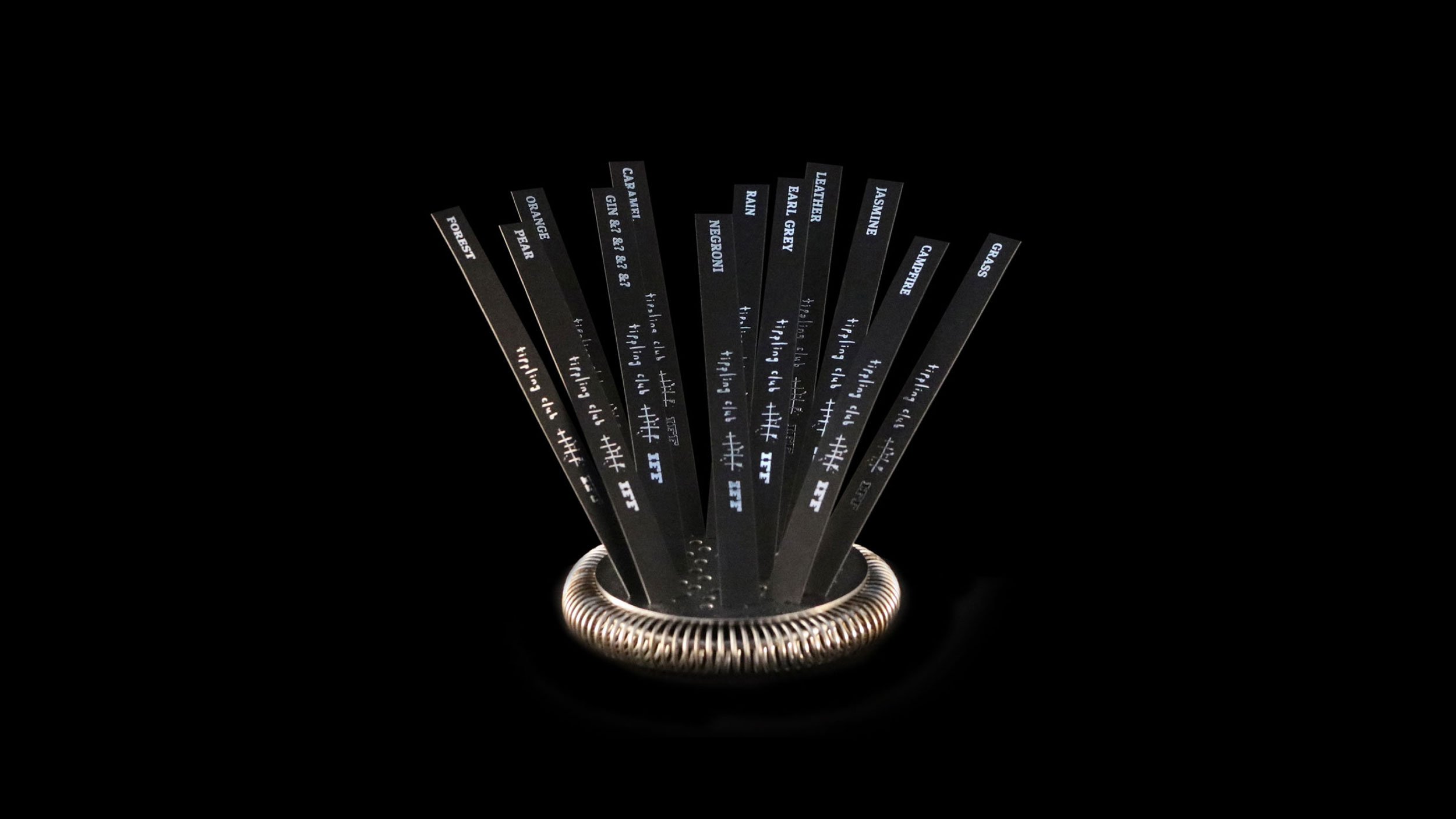 Sensorium menu: triggering memories through aroma, circa 2016. This cocktail menu takes the form of black perfume test strips with the cocktail name foiled in silver on each one, presented fanned out on a silver cocktail strainer.