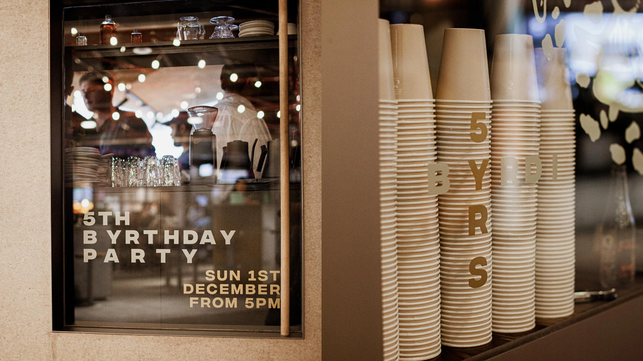 Side-by-side photos showing the 5th birthday party decals on the Byrdi windows. Typography on the Byrdi door (left image) and BYRDI 5 YRS logo lockup on a window (right image).
