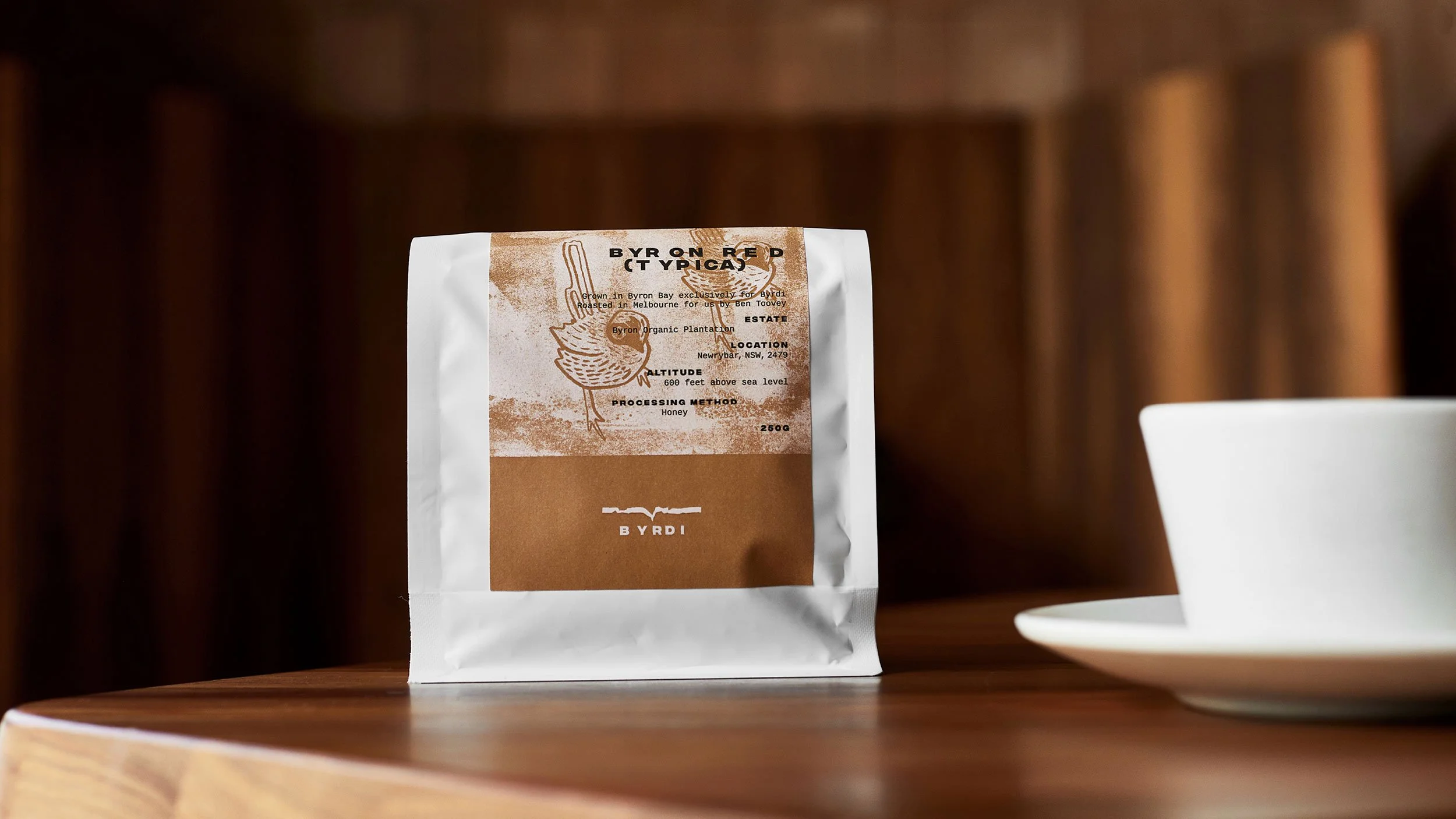Byrdi coffee packaging sitting on a wooden table next to a coffee cup.