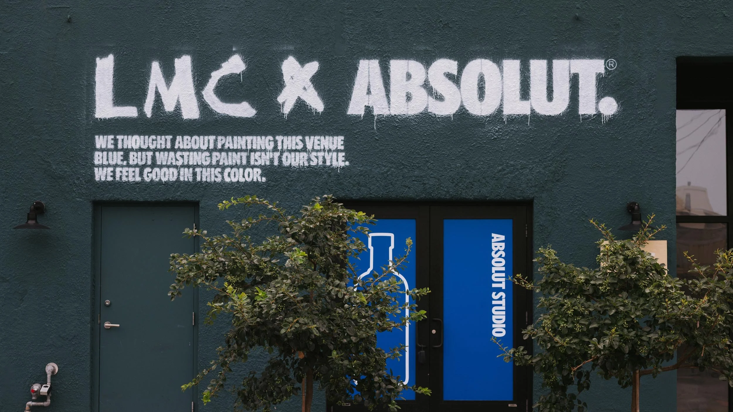 LMC x Absolut logo lockup spray painted onto the side of dark green building in New Orleans. Blue double doors feature silhouette of an Absolut bottle and the words Absolut Studio.