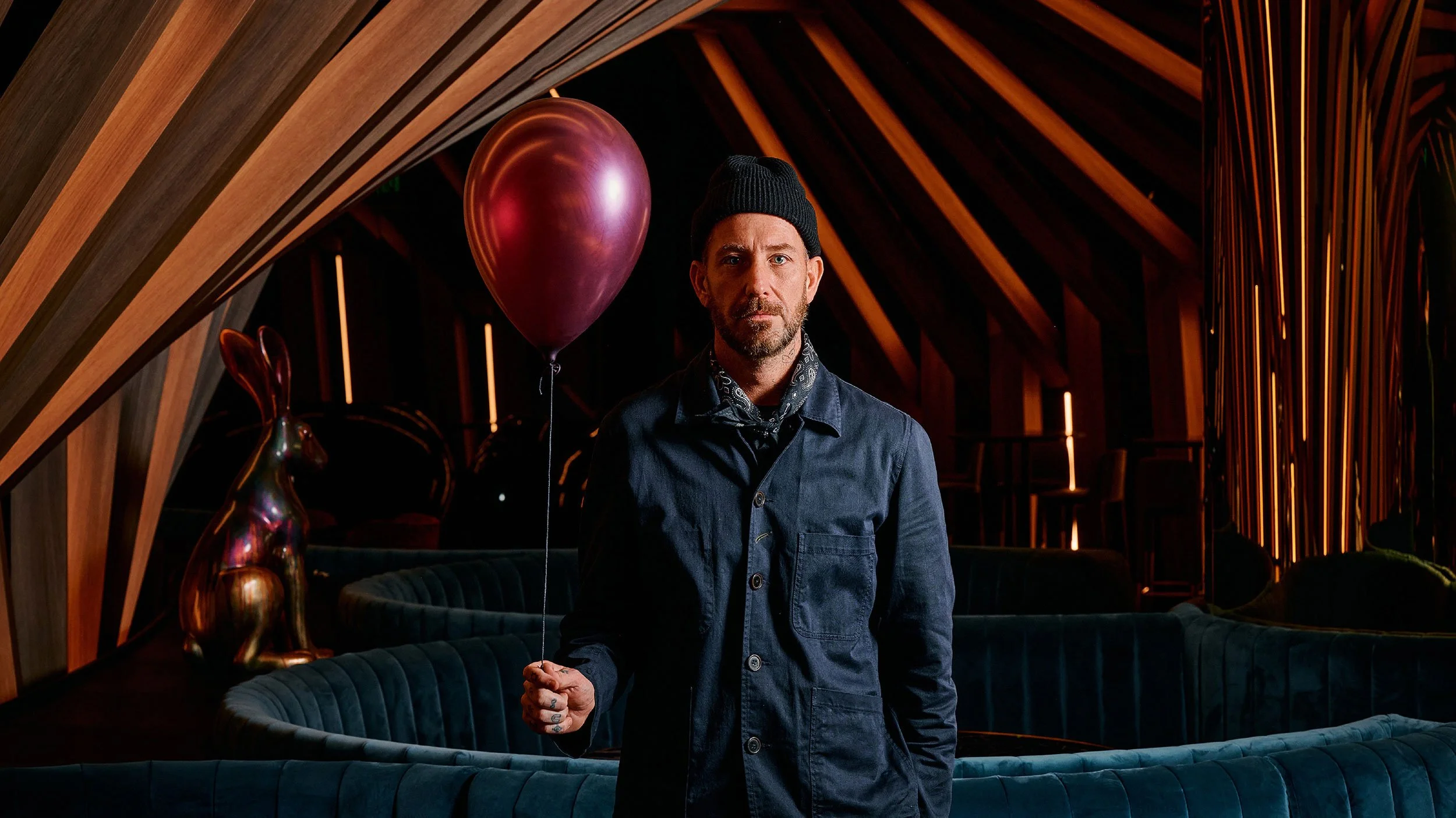 Matt Whiley, in a black beanie and navy blue shirt stands holding a maroon balloon at the Curious Bar at W Melbourne.