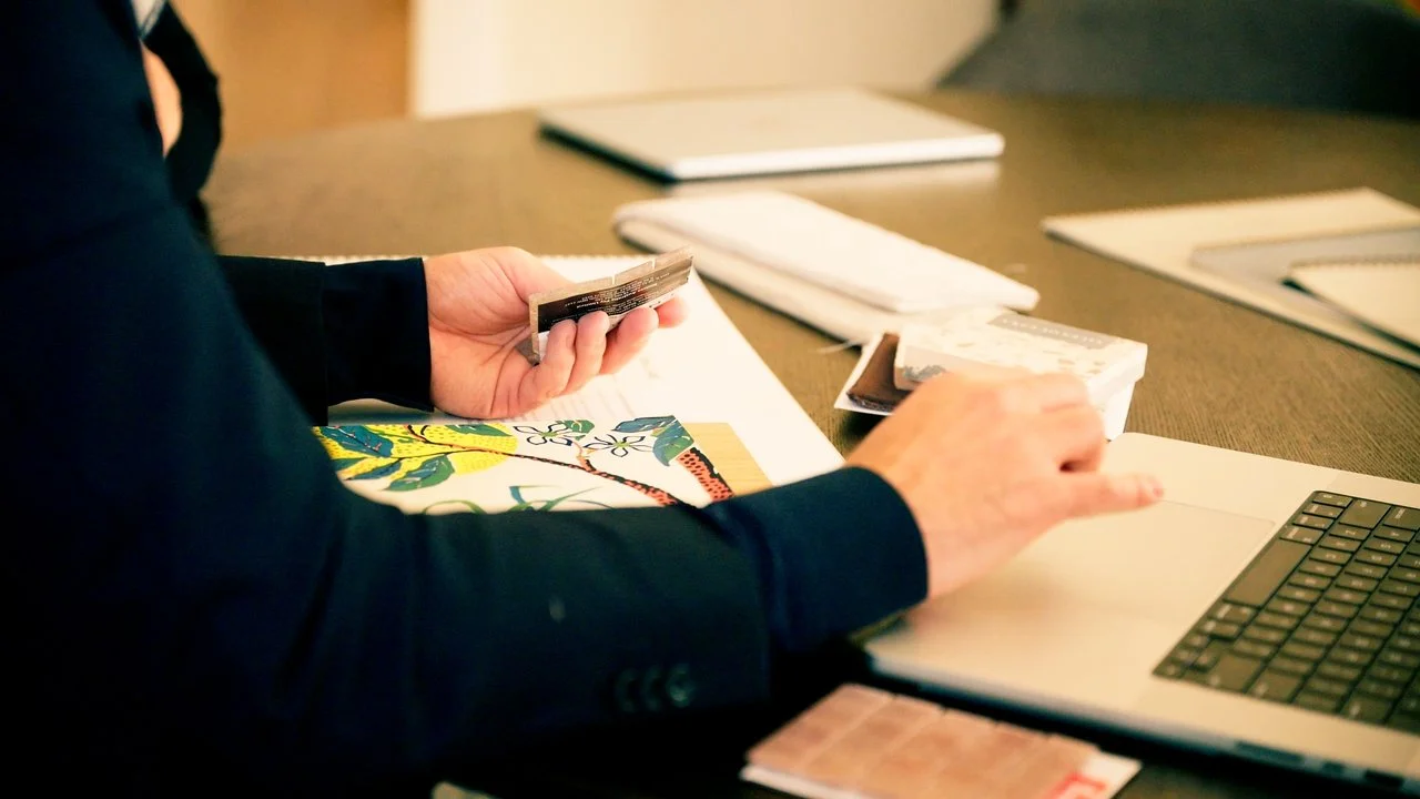 Person working at a desk with a laptop, papers, notebooks, and fabric swatches